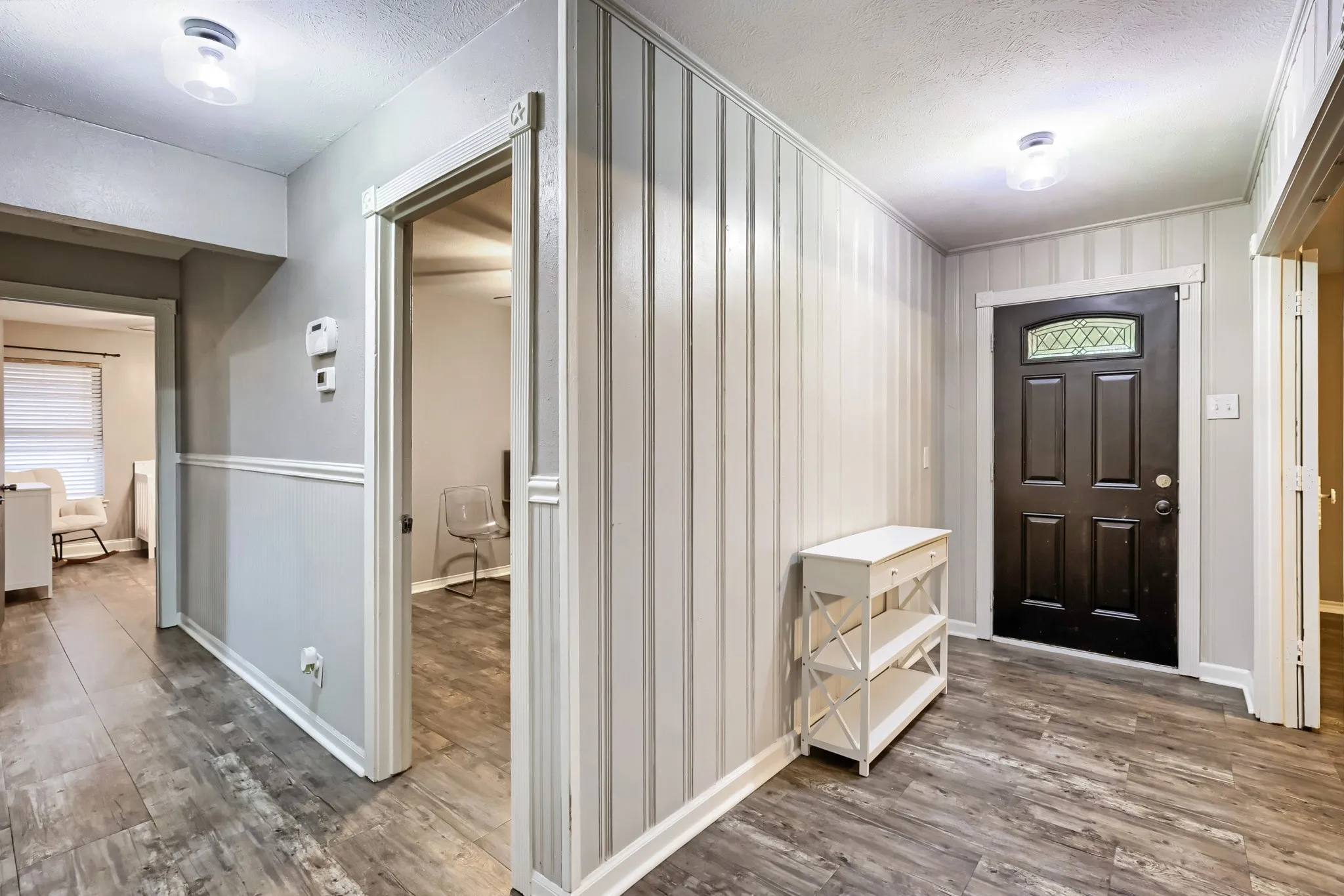 Wood-finish flooring throughout, beadboard wall paneling, and an entry door with leaded glass details