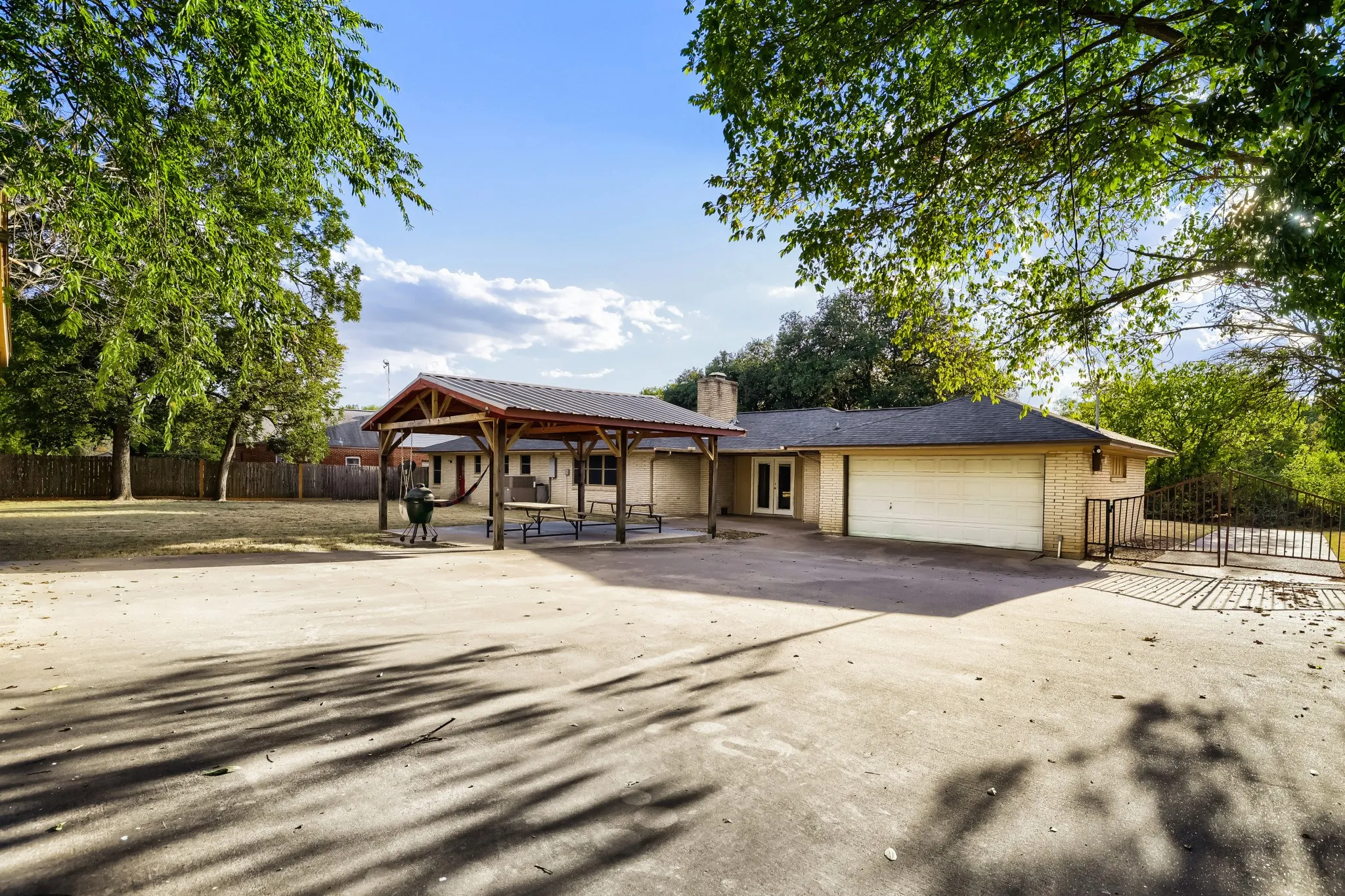 Expansive concrete pad, covered outdoor structure, attached two-car garage, and mature trees