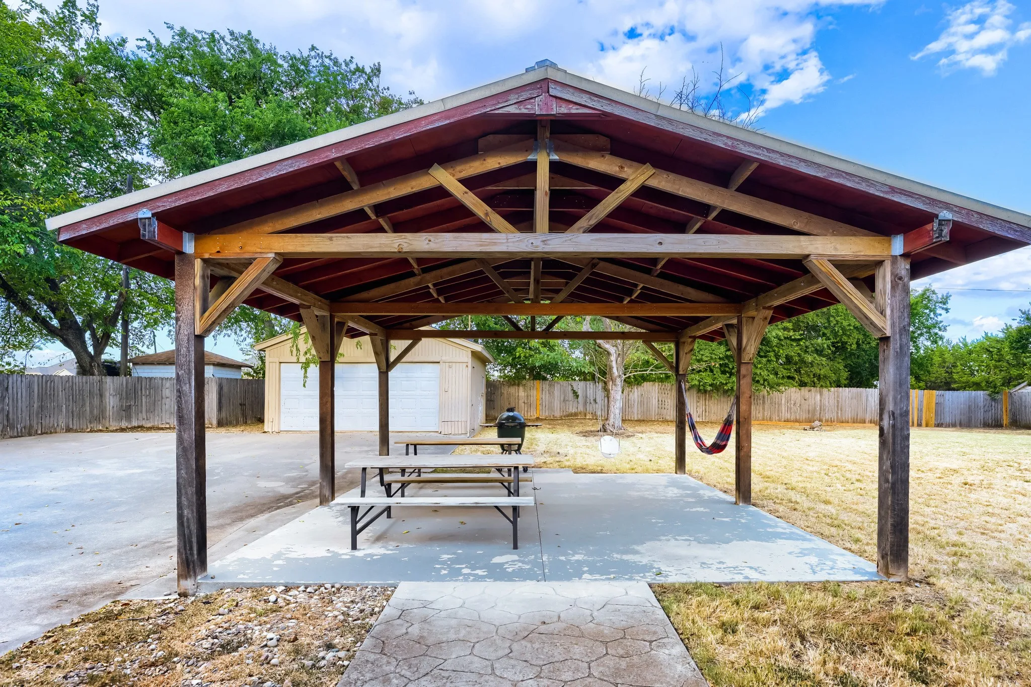 Expansive outdoor covered patio structure with exposed wood beam ceiling, concrete flooring, and an adjoining detached two-car garage