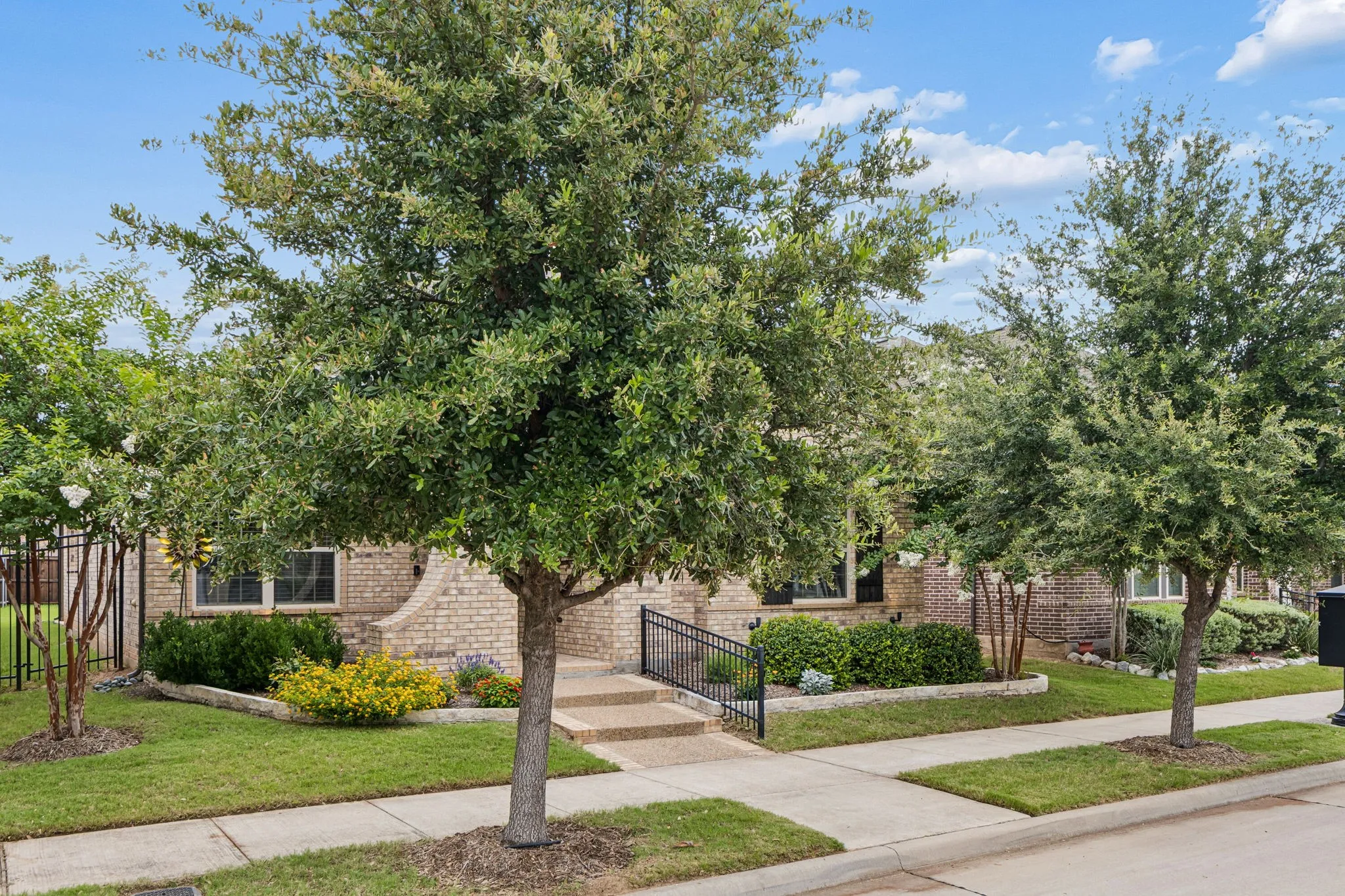 Brick exterior with mature trees, landscaped planting beds, and a concrete walkway