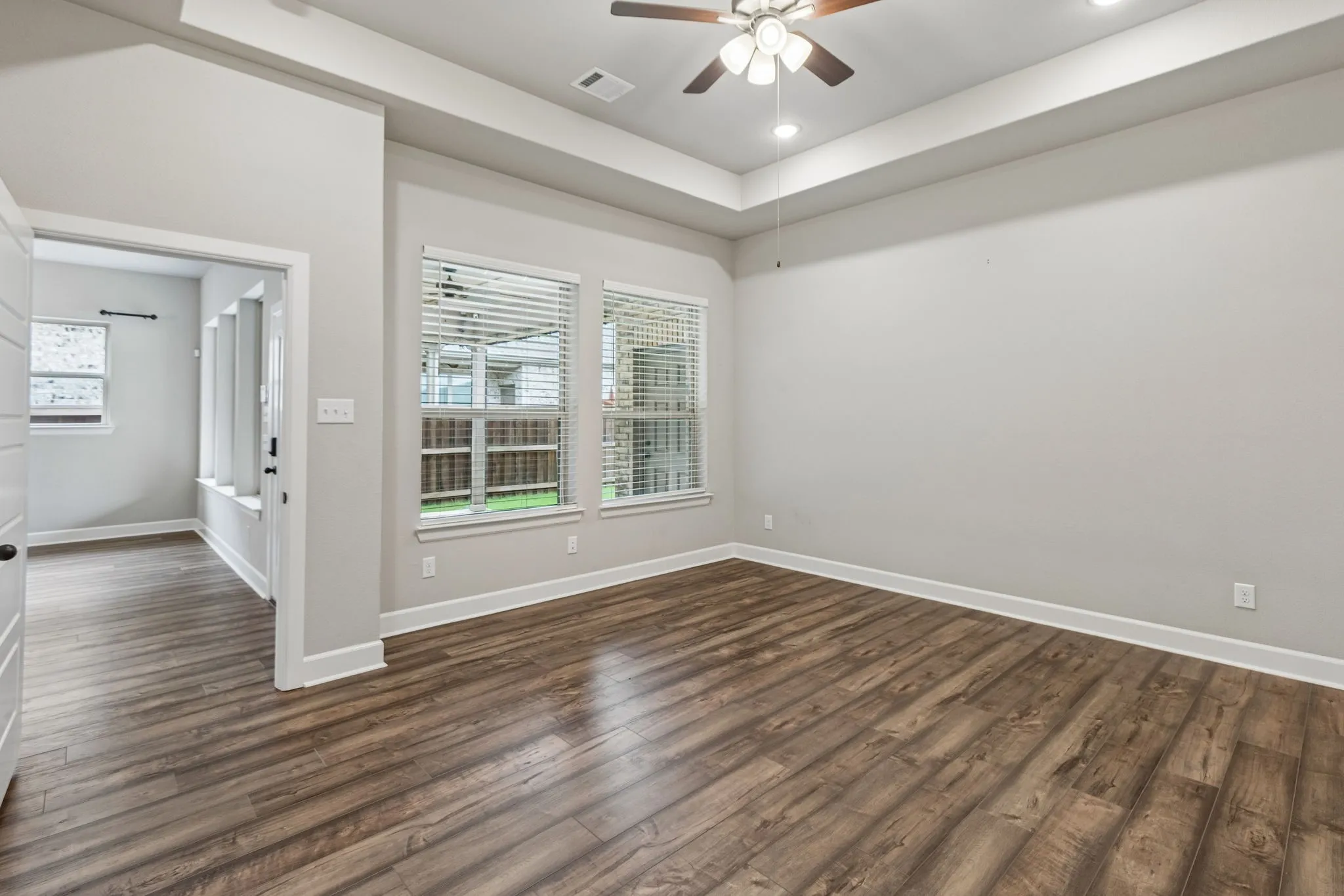 Tray ceiling with recessed lighting, wood-finish flooring, ceiling fan, and multiple windows