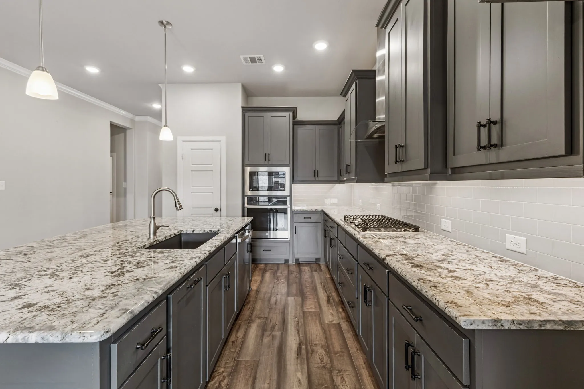 Kitchen featuring an expansive island with a built-in sink, stone countertops, gray cabinetry, and wood-finish flooring