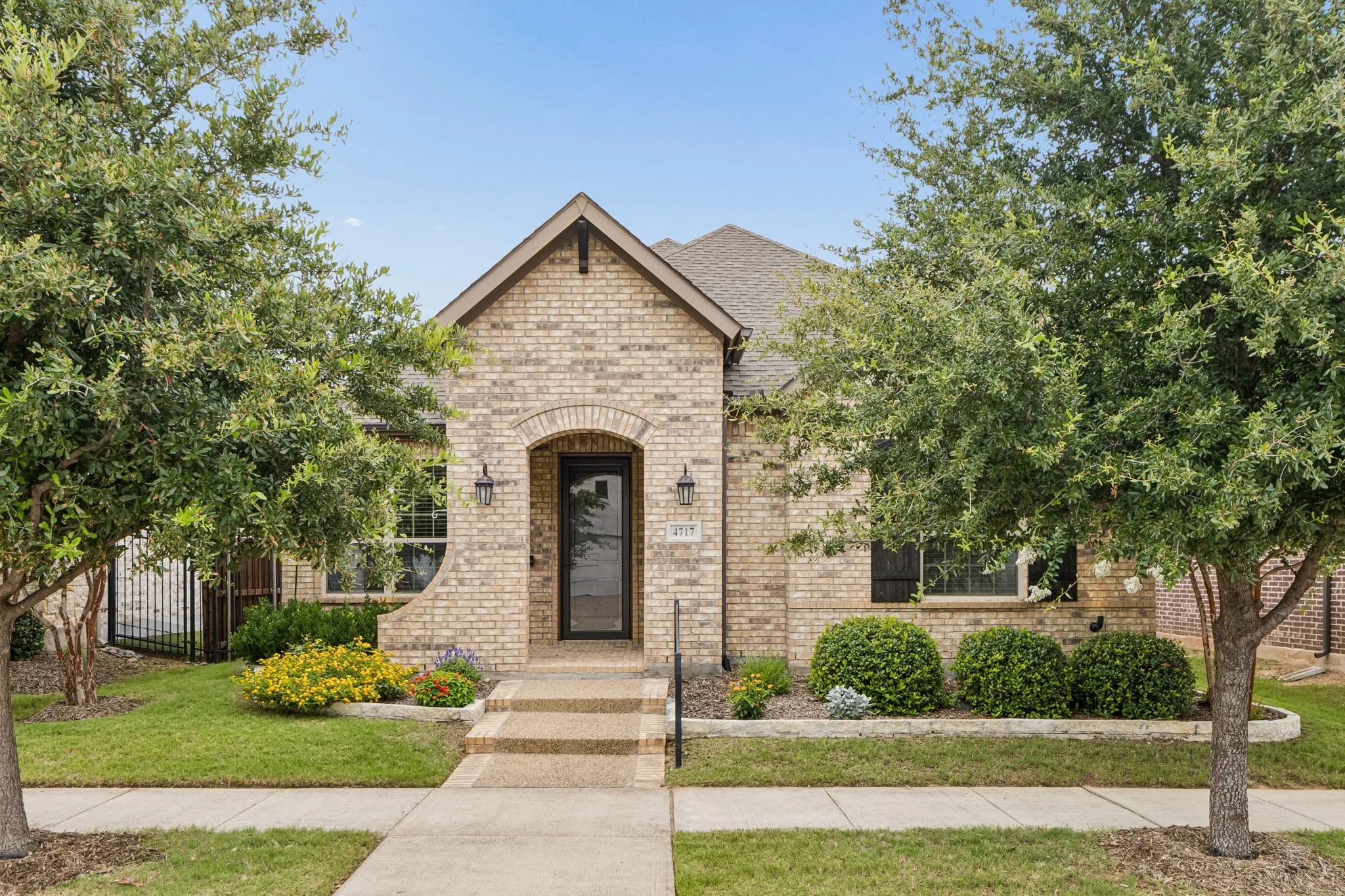 Brick exterior with an arched entryway, established landscaping, concrete pathway, and a covered porch