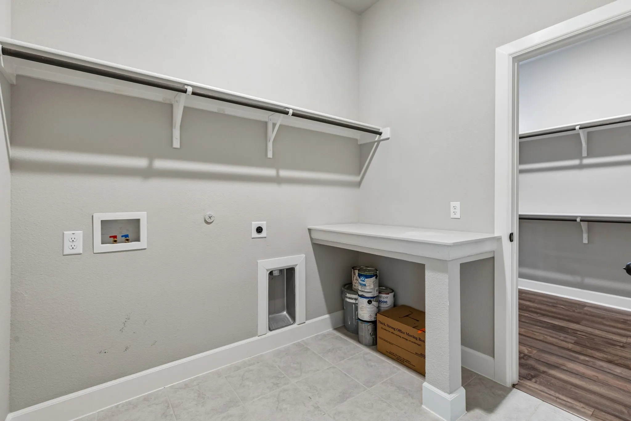 Built-in shelving with hanging rods, laundry connections, white baseboards, and a built-in folding counter