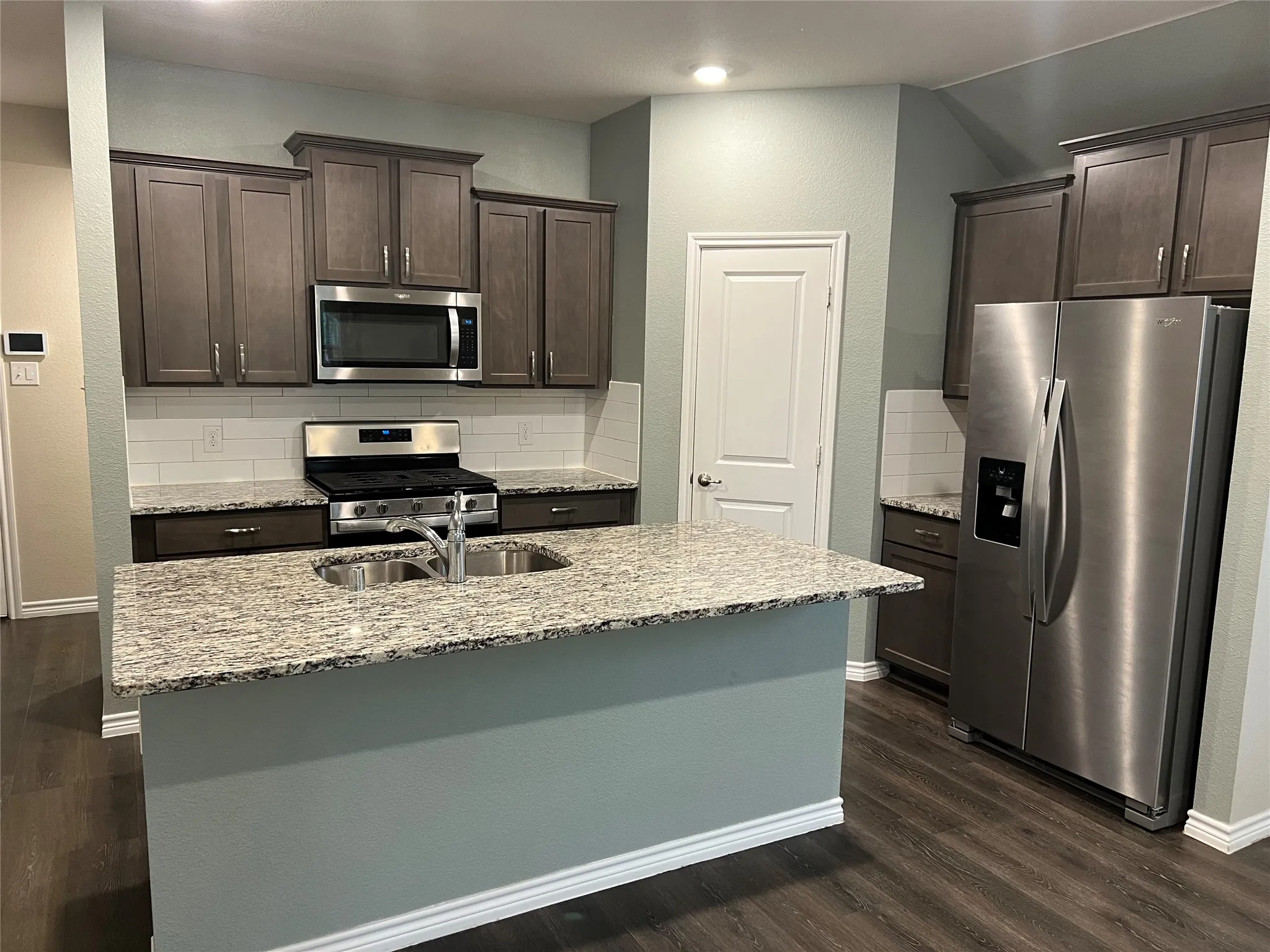 Kitchen featuring a kitchen island with sink, dark wood-type flooring, backsplash, and appliances with stainless steel finishes