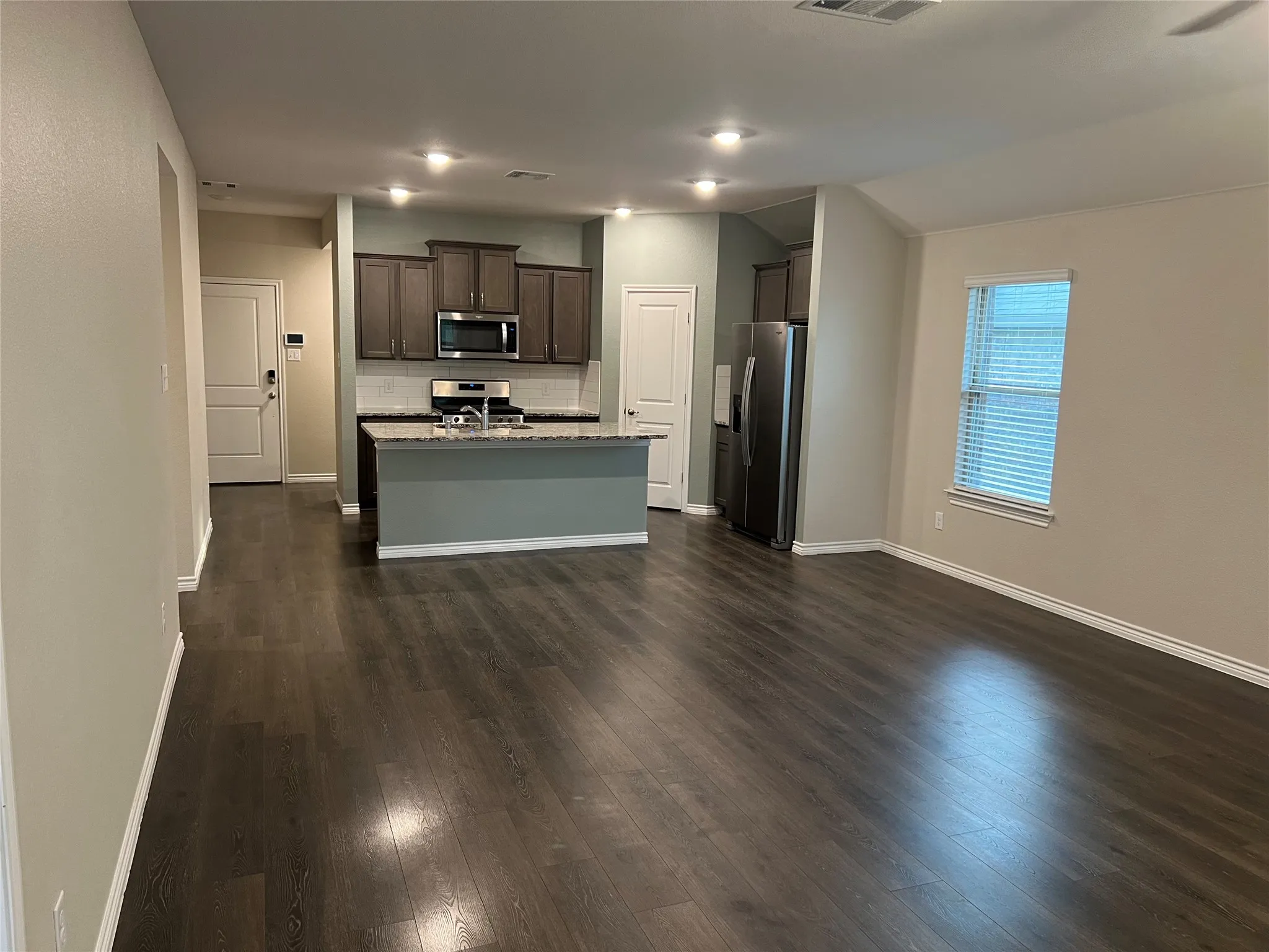 Kitchen featuring tasteful backsplash, dark brown cabinetry, dark hardwood / wood-style flooring, a kitchen island with sink, and appliances with stainless steel finishes