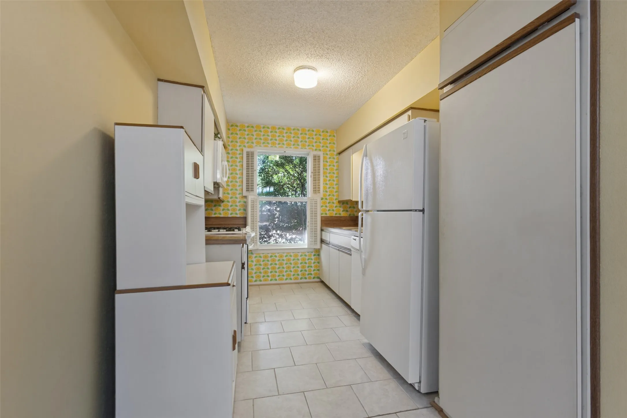 Galley kitchen with white appliances, white cabinetry, a window, and tiled flooring