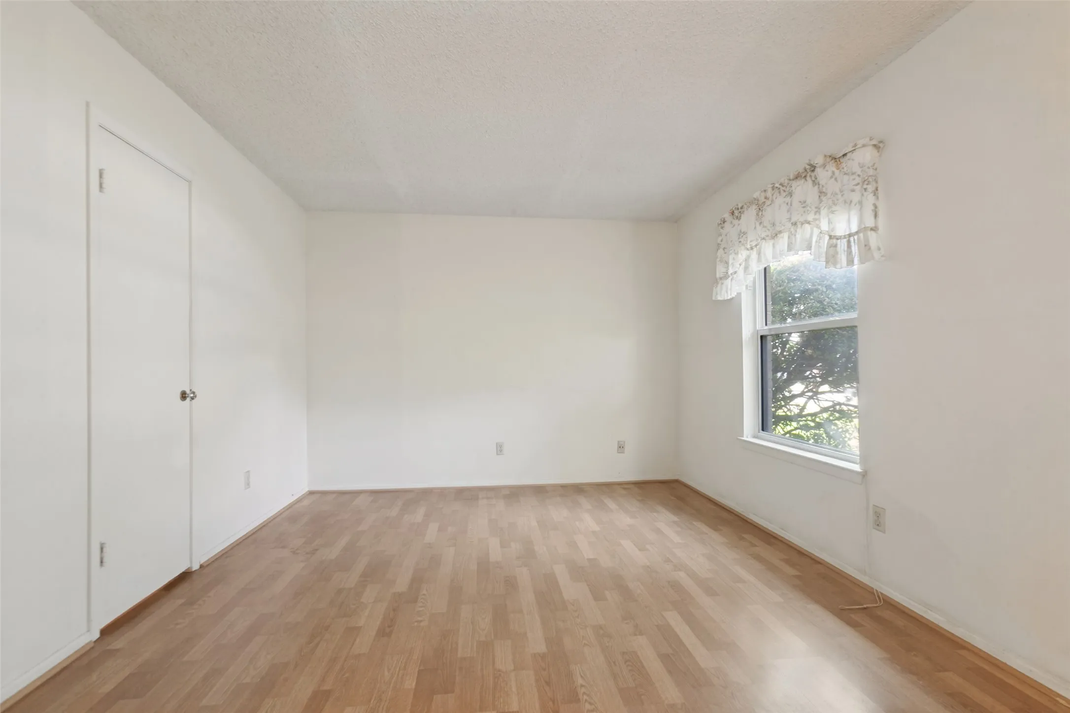 Wood-finish flooring with white walls and a single window