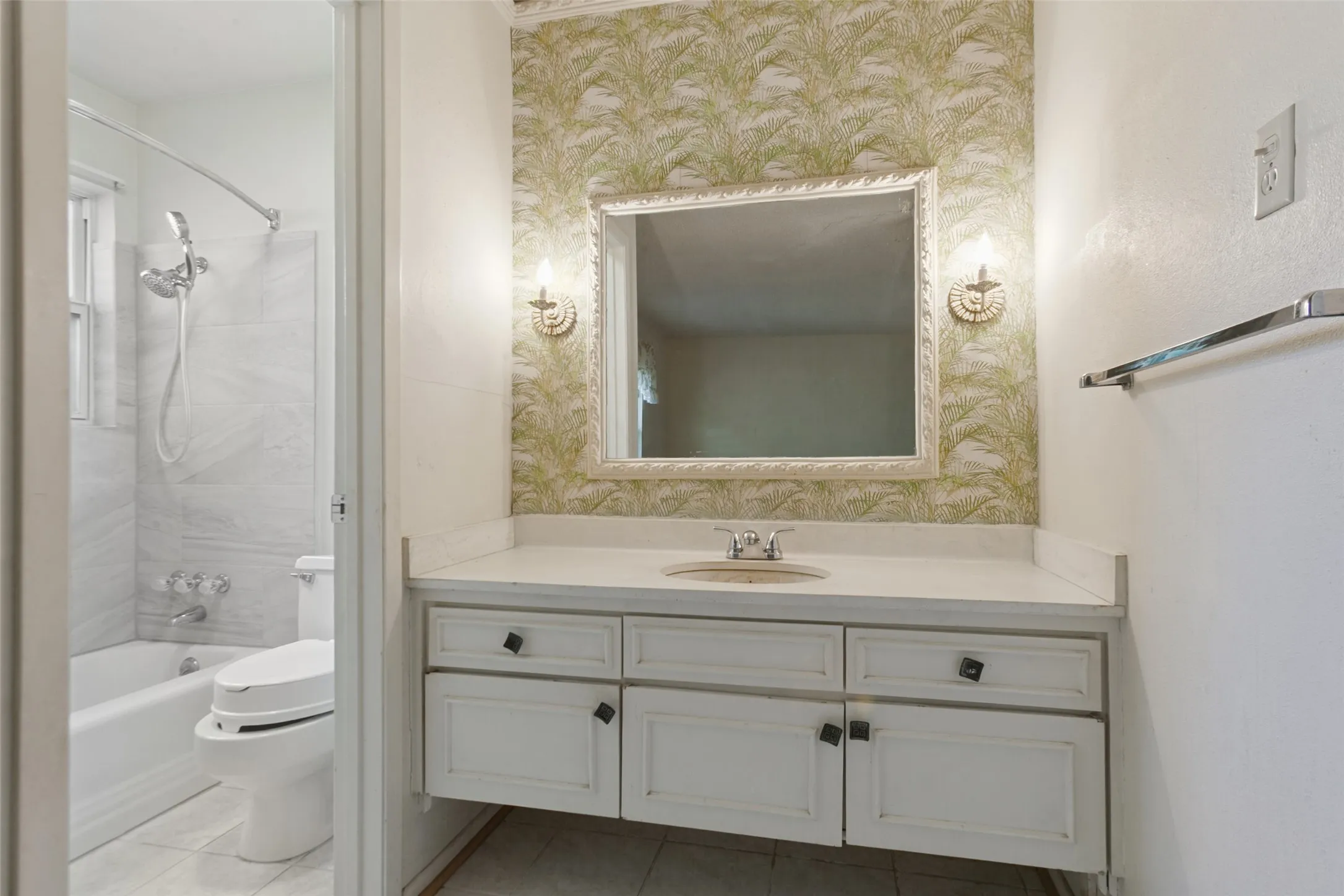 Vanity with an integrated sink, framed mirror, wall sconces, and patterned wallpaper
