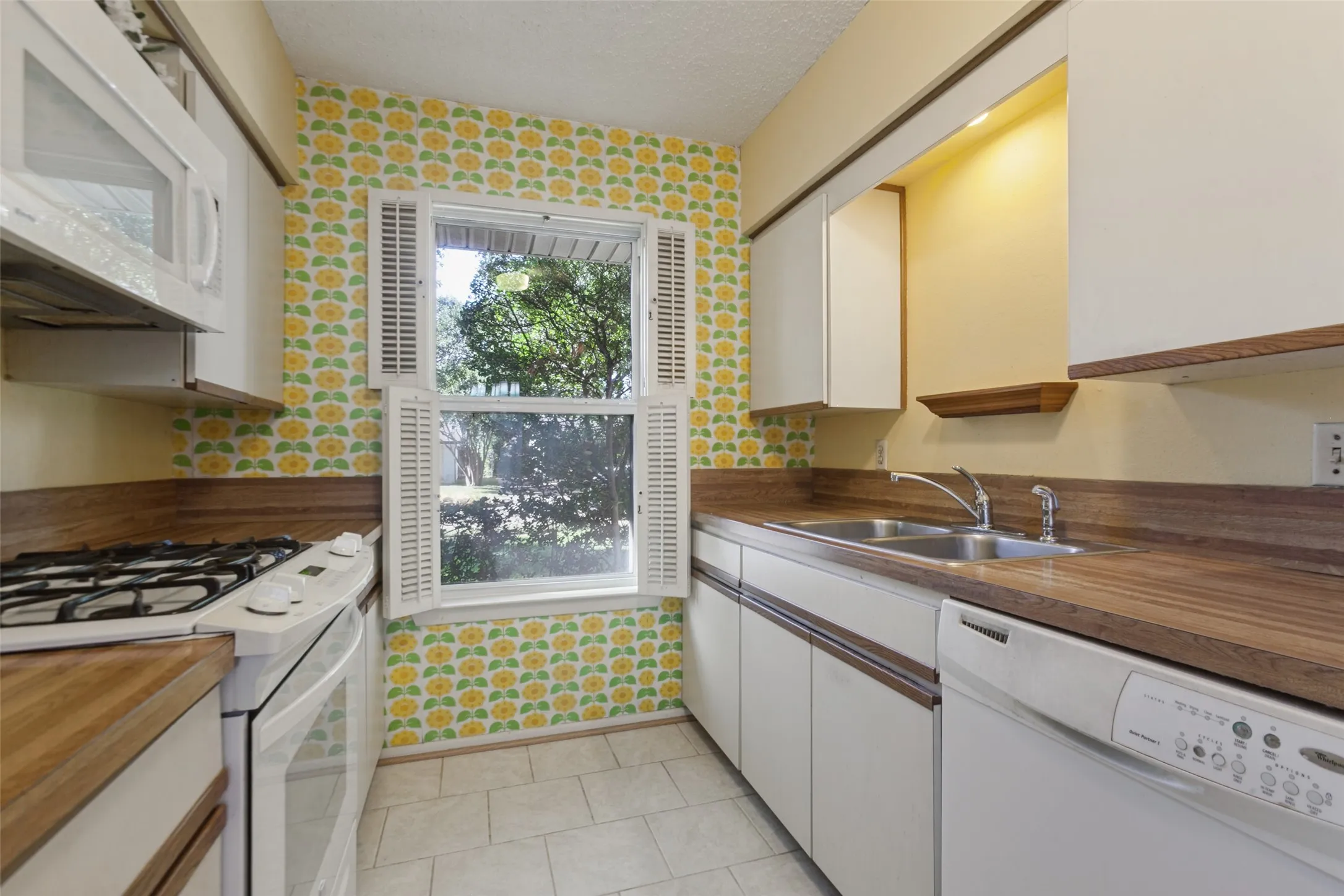 Kitchen featuring wood-finish countertops, white cabinetry, a built-in microwave, and a double-basin stainless steel sink