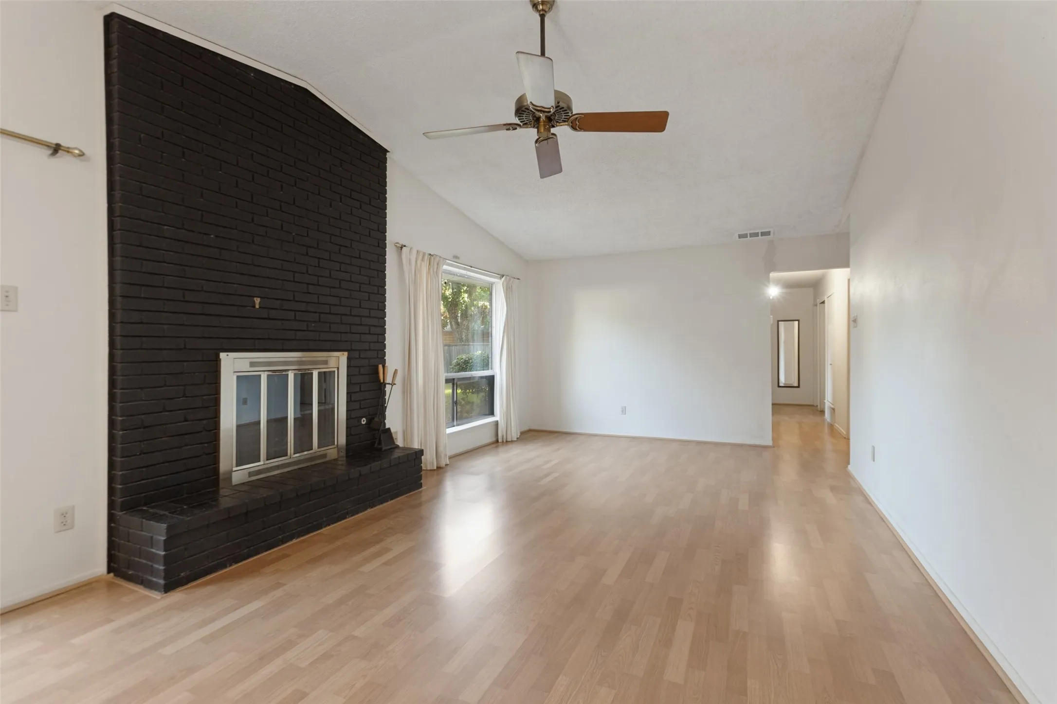 Spacious living area featuring a black brick fireplace, wood-finish flooring, vaulted ceiling, and a ceiling fan