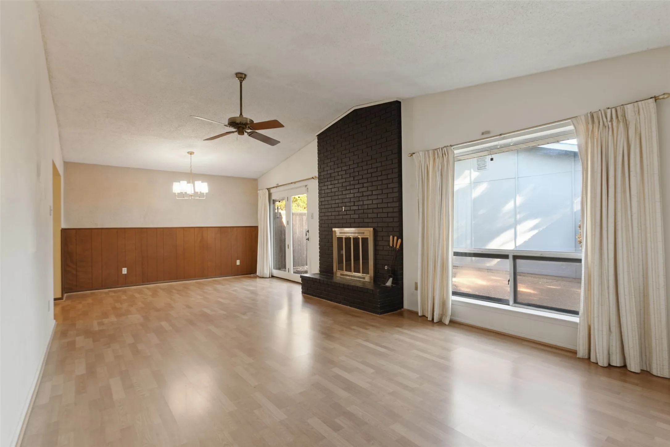 Wood-finish flooring, dark brick fireplace with metal insert, vaulted ceiling, ceiling fan, and sliding glass door