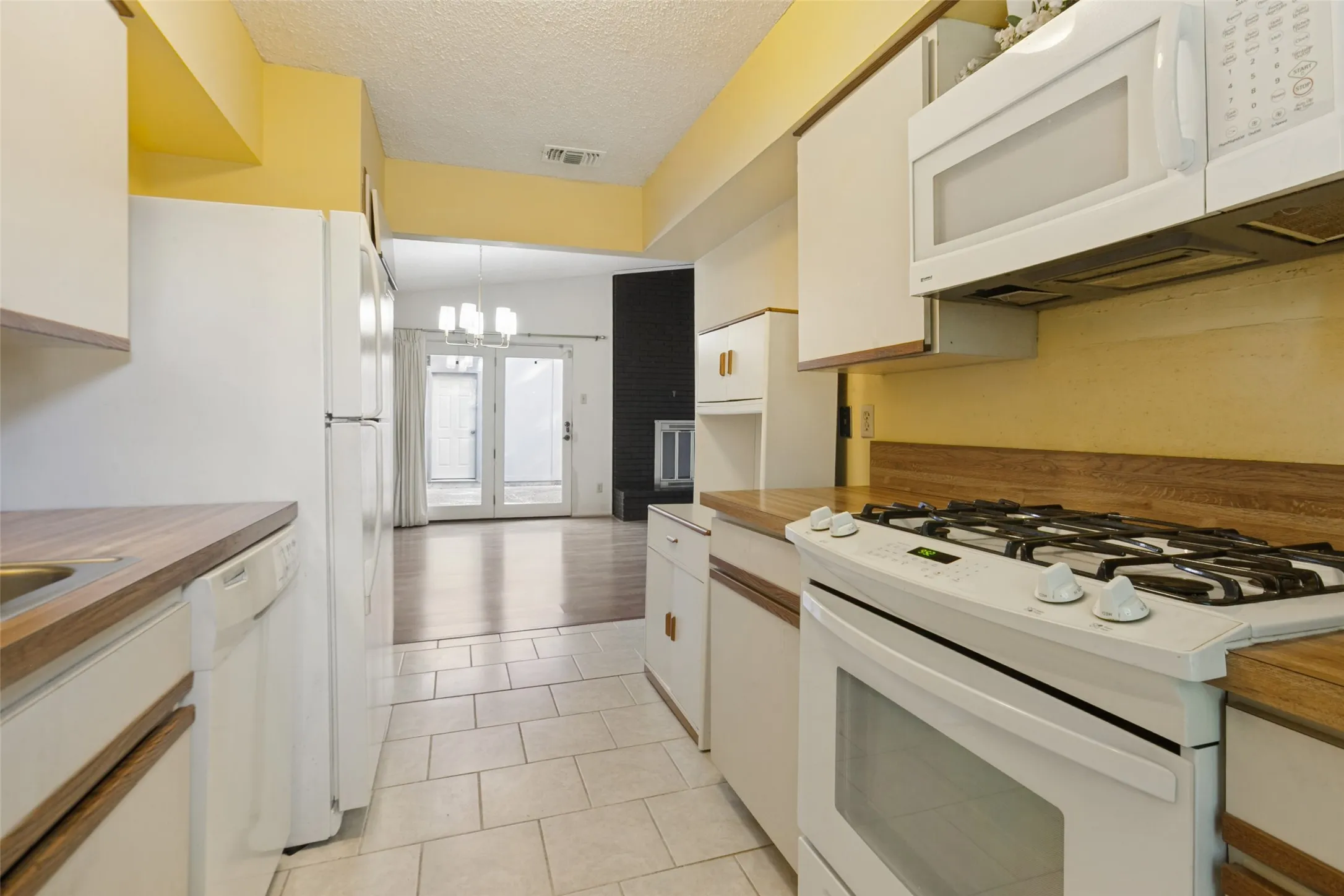 Galley kitchen featuring white cabinetry, wood-finish countertops, tile flooring, and white appliances including a gas range and built-in microwave