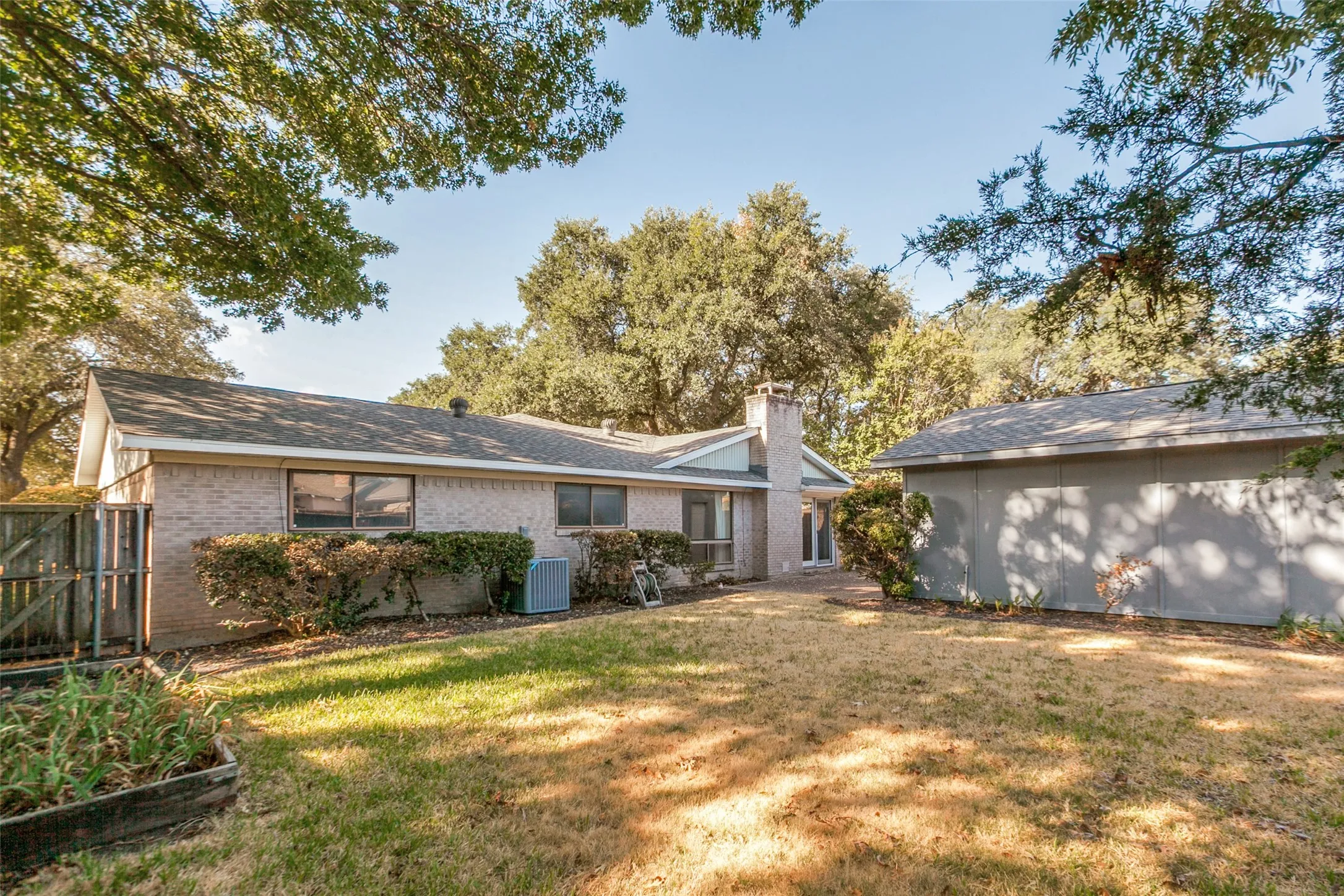 Rear exterior featuring brick siding, a privacy fence, a detached shed, and a raised garden bed