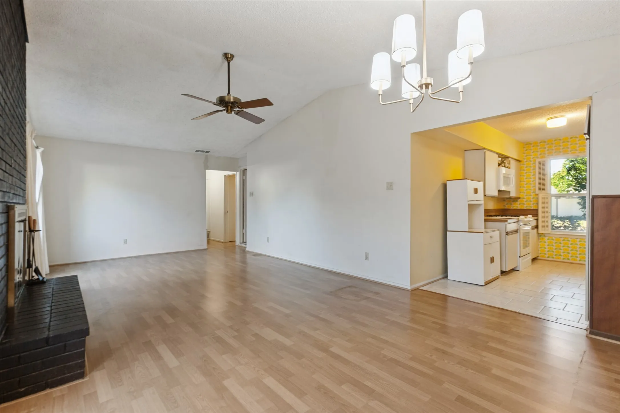 Vaulted ceiling with a ceiling fan, wood-finish flooring, black brick fireplace, and an arched doorway leading to the kitchen with built-in cabinetry