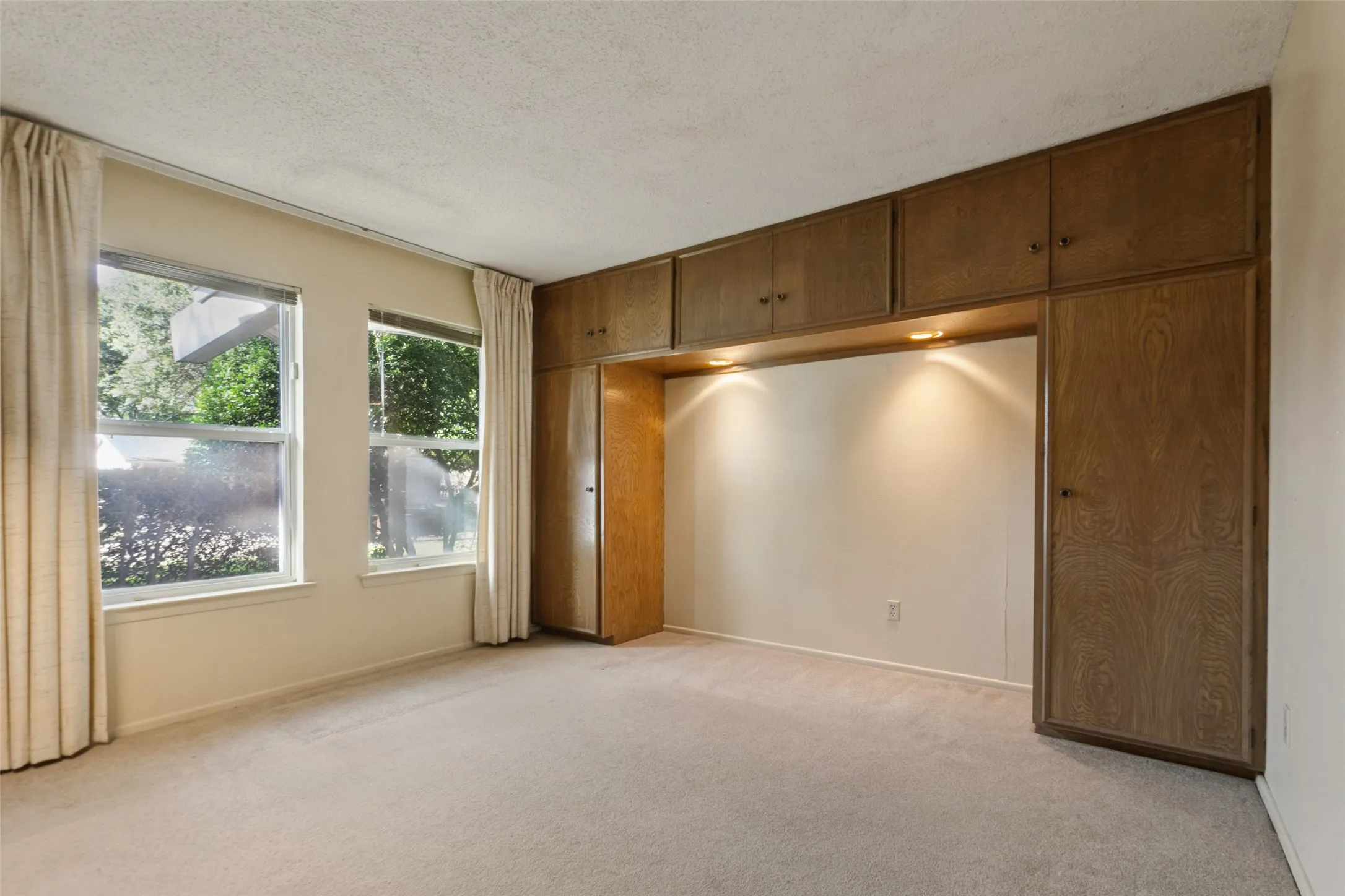 Built-in wood-finish cabinetry with integrated lighting, two double-hung windows, and light-toned carpet