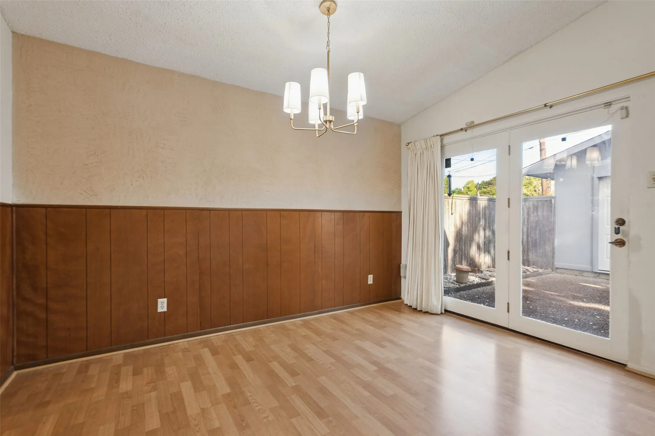 Wood-finish flooring, paneled wall detailing, brass finish chandelier, and double patio doors