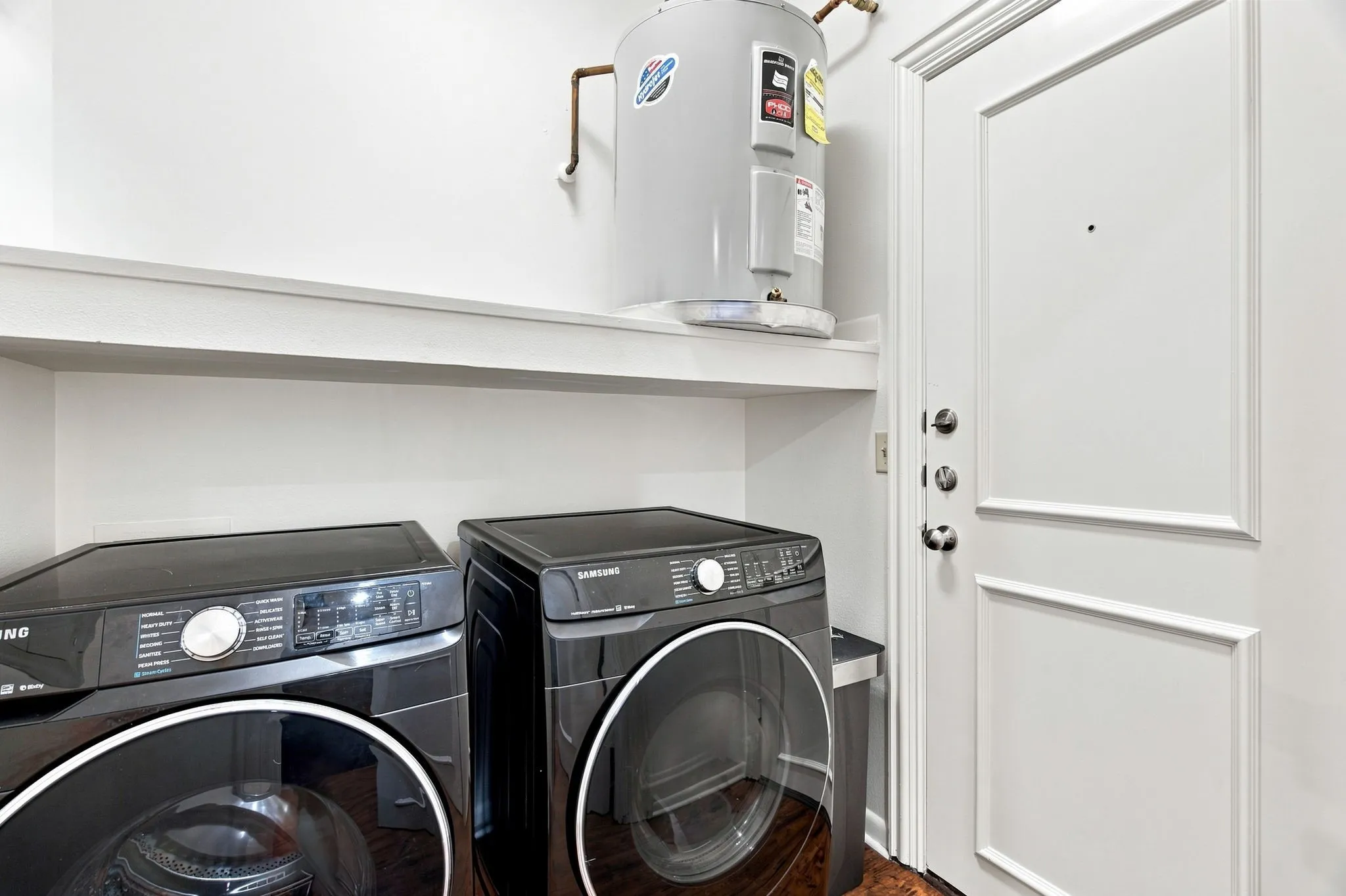 Laundry area with a water heater, built-in shelving, and wood-finish flooring