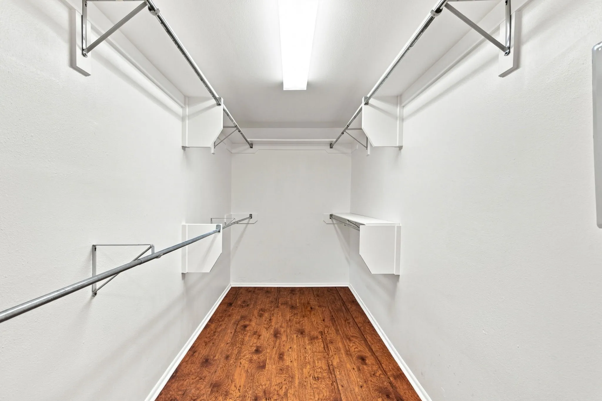 Walk-in closet featuring wood-finish flooring, white walls, built-in shelving, and metal hanging rods