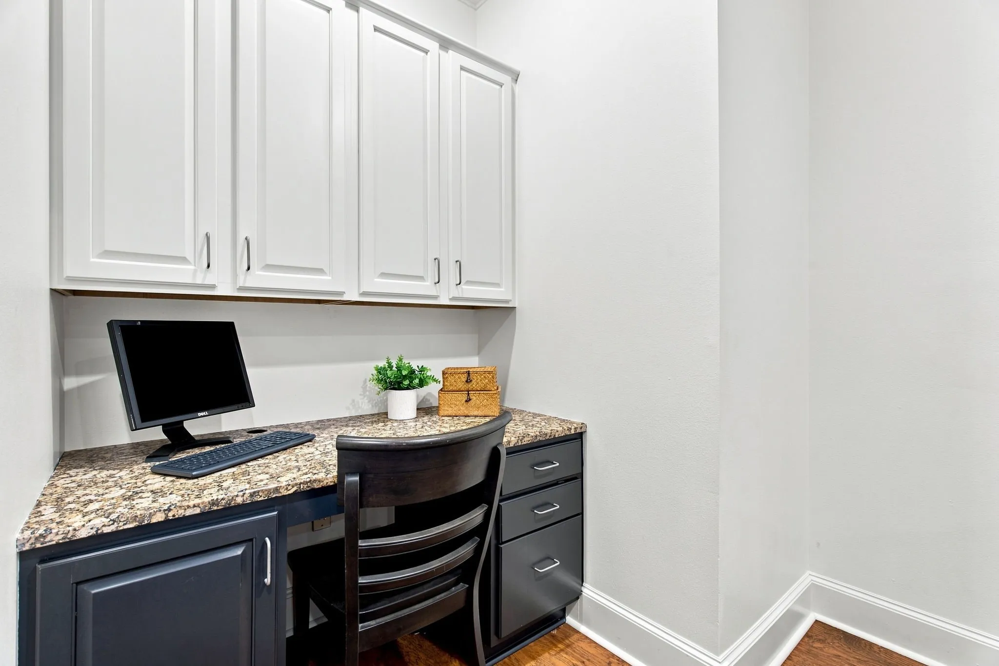 Built-in desk with a stone-finish countertop, white upper cabinetry, dark lower cabinetry, and wood-finish flooring off of the breakfast nook.