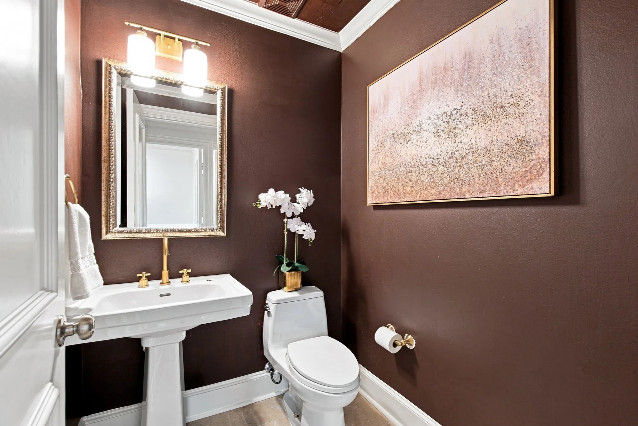 Half bathroom adjacent to living room with a eedestal sink with brass-finish faucet, framed mirror, and wall-mounted vanity light.