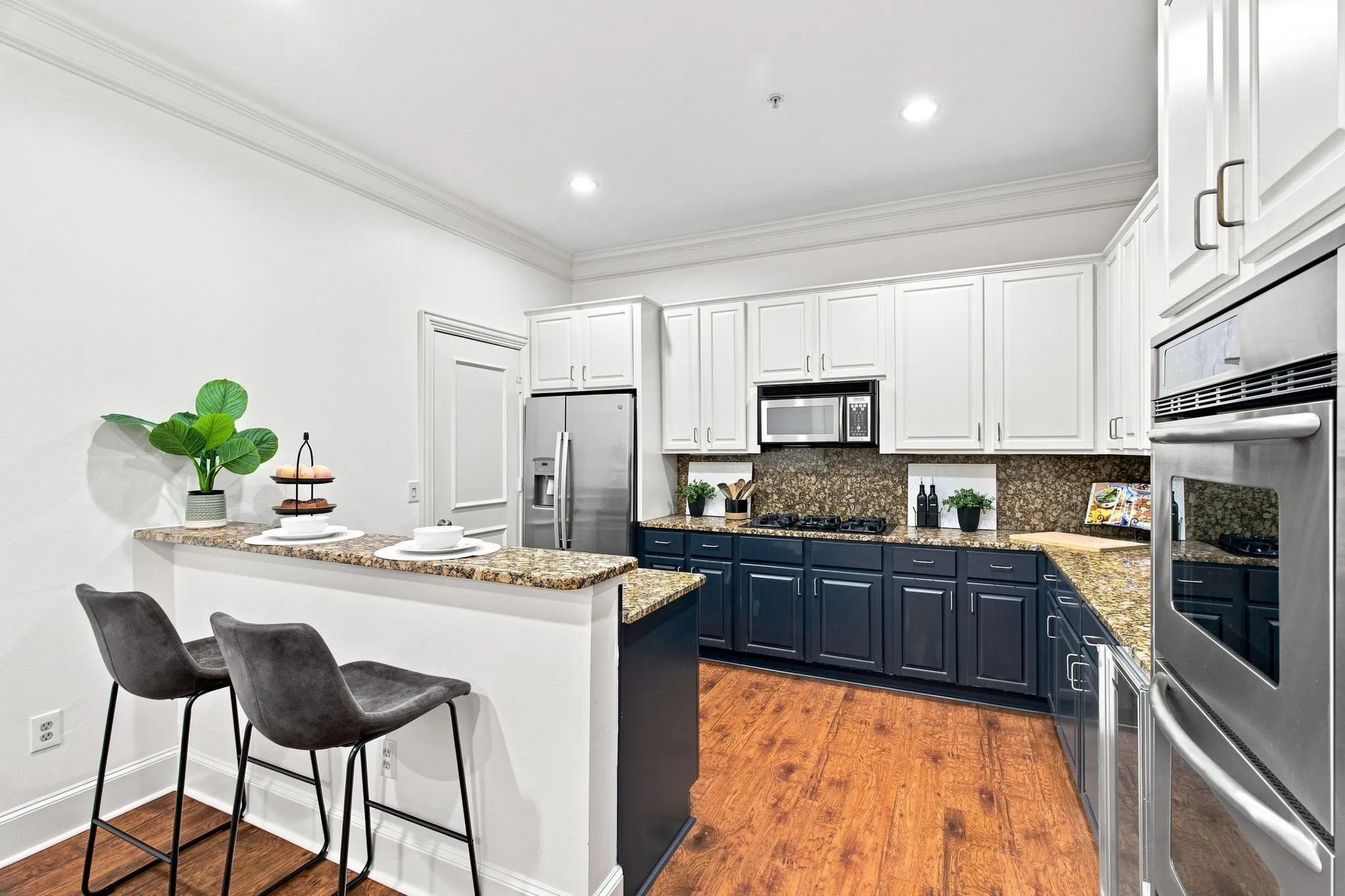 Kitchen featuring wood-finish flooring, two-tone cabinetry, stainless steel appliances, granite countertops, and recessed lighting