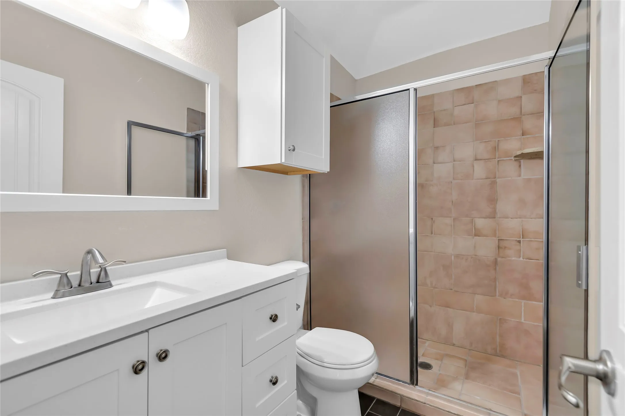 Bathroom featuring a white vanity with integrated sink, brushed nickel faucet, a framed mirror, and a shower with tiled walls and a glass enclosure