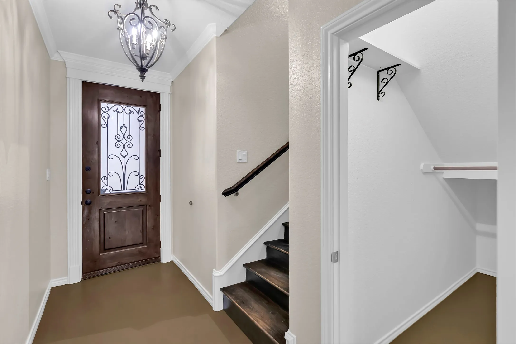 Dark wood entry door with decorative ironwork, wrought iron chandelier, wood-finish stairs, and under-stair storage