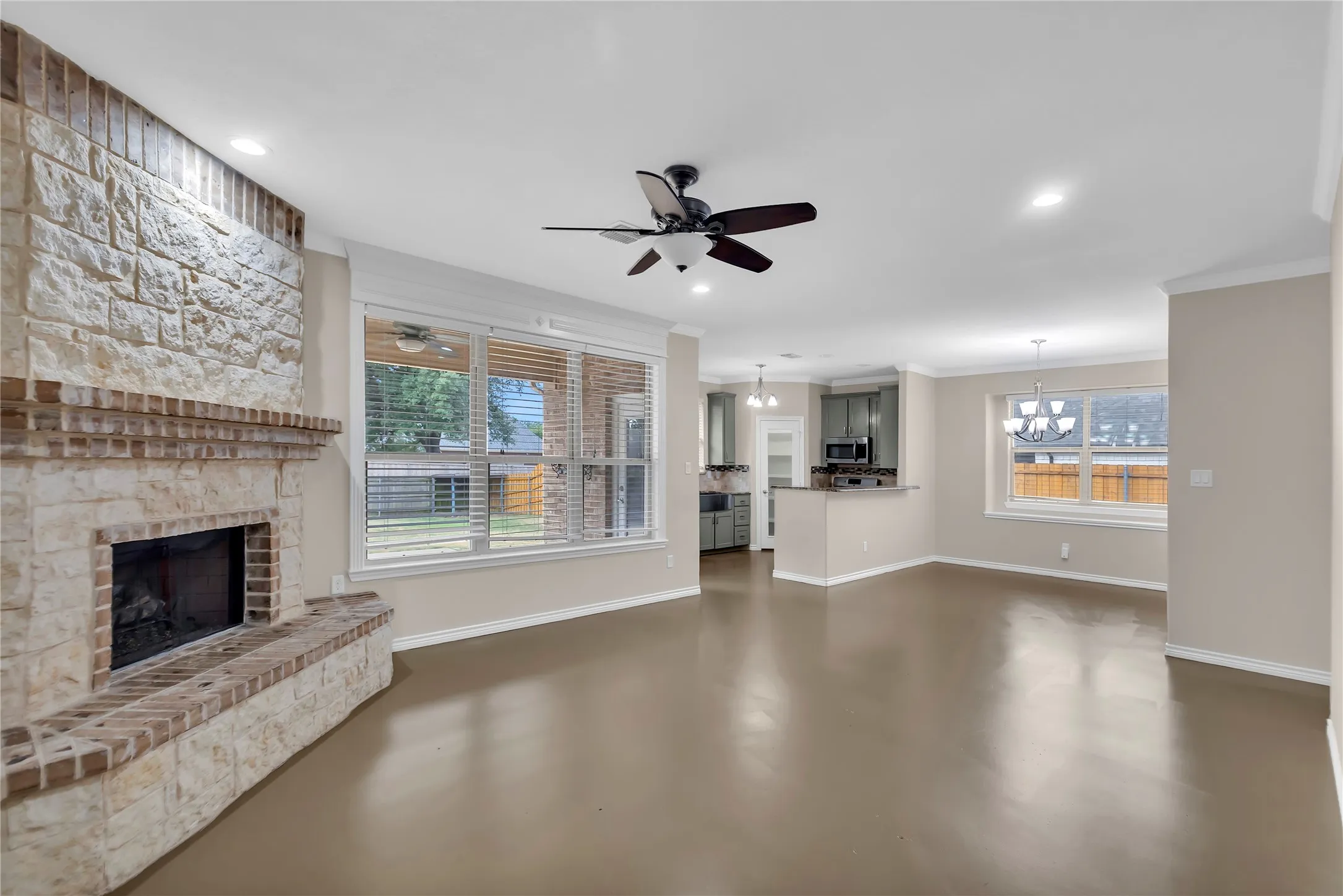 Stone fireplace with brick hearth, large windows with blinds, recessed lighting, ceiling fan, and wood-finish flooring