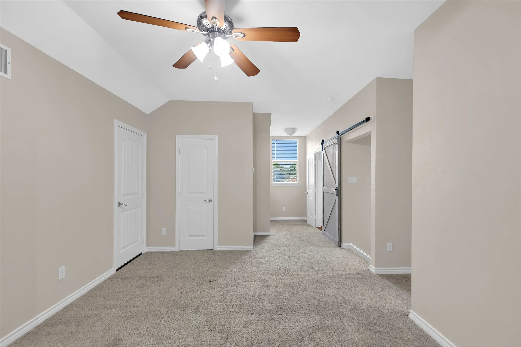 Vaulted ceiling with a ceiling fan, plush carpet flooring, and a barn-style sliding door