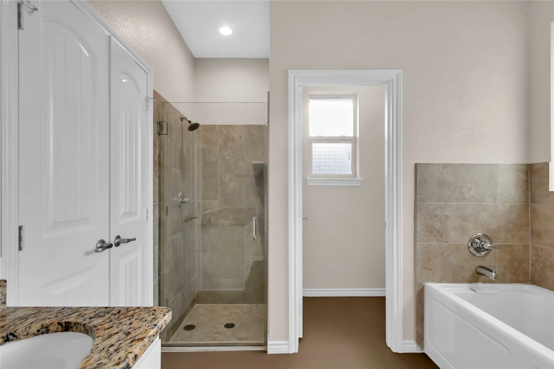 Walk-in shower with glass enclosure, separate bathtub, and granite-finish countertop