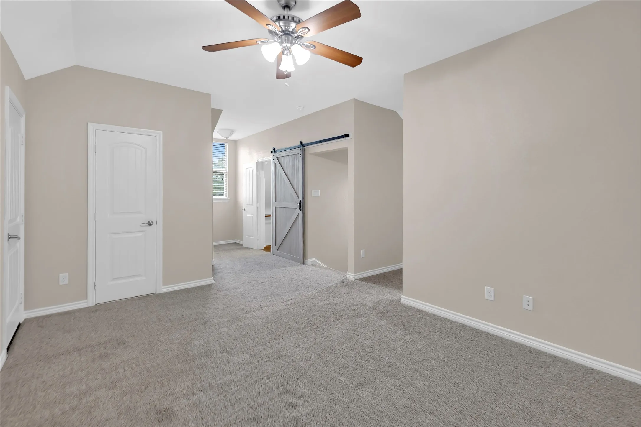 Spacious room with vaulted ceilings, a ceiling fan, light gray carpeting, and a barn door