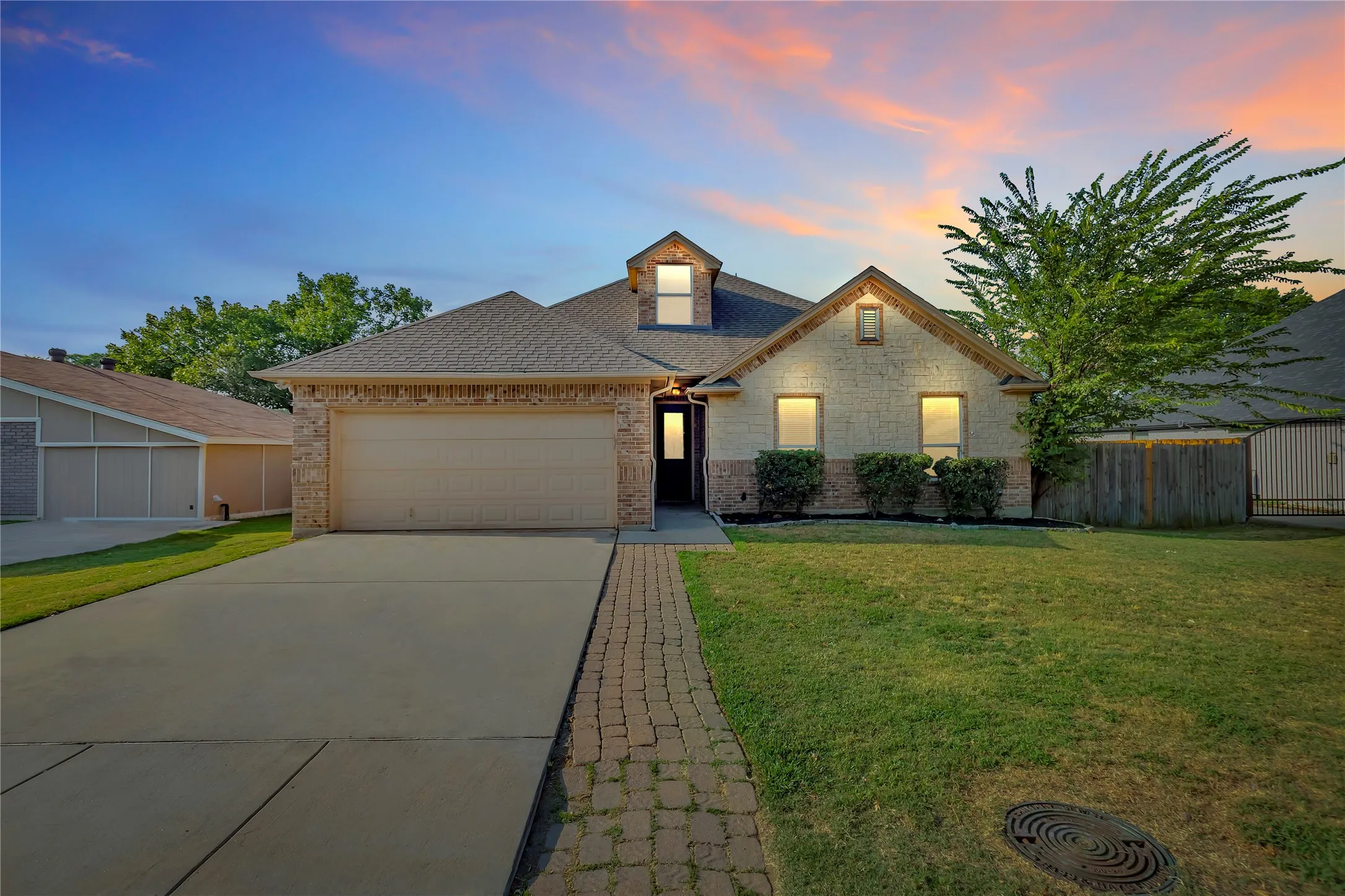 Brick and stone exterior with a dormer window, an attached garage, a concrete driveway, and a paver walkway