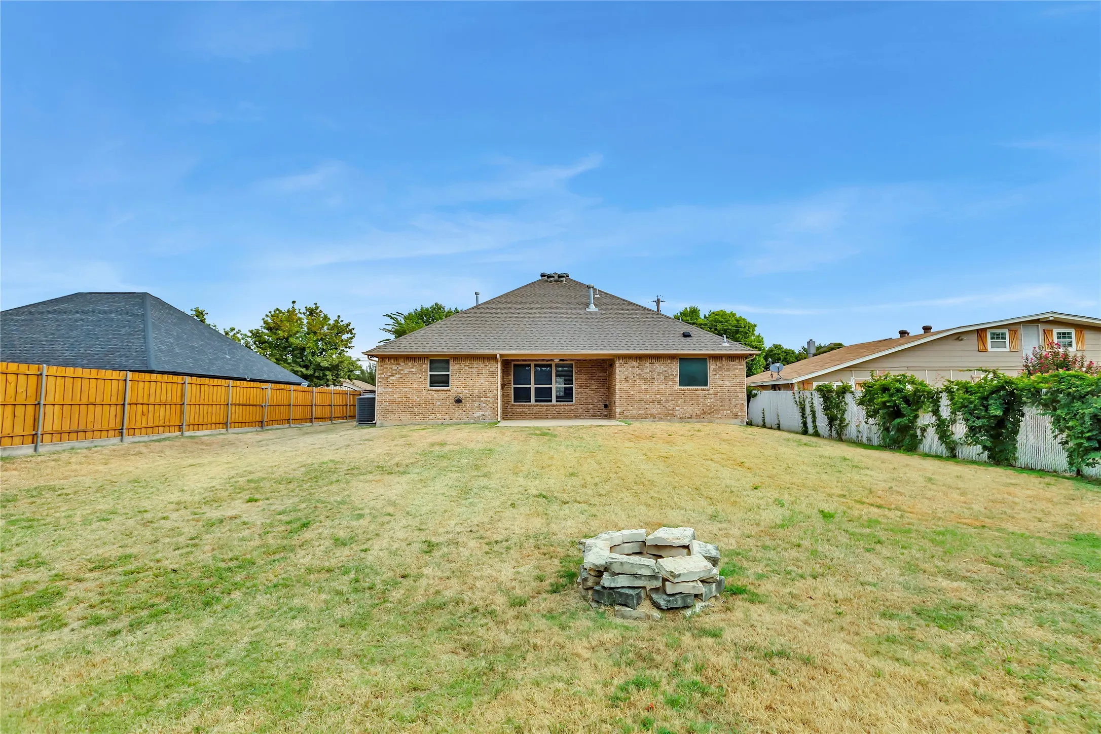 Expansive backyard featuring a stone fire pit, wood privacy fence, and brick exterior