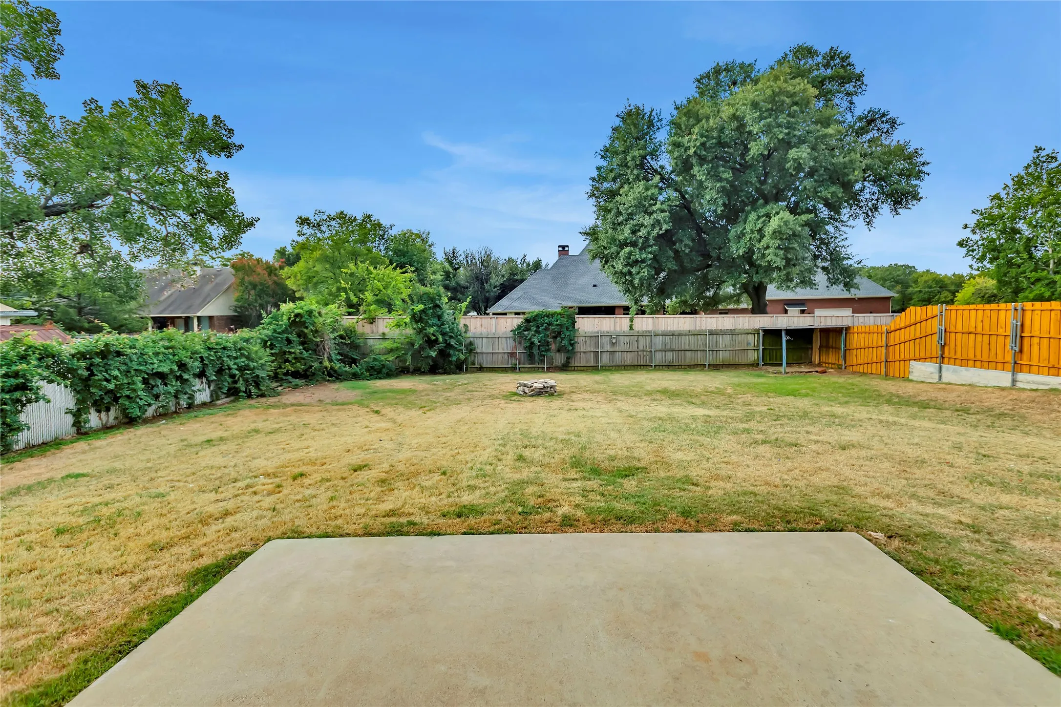 Expansive backyard featuring a concrete patio, wood privacy fencing, and mature trees