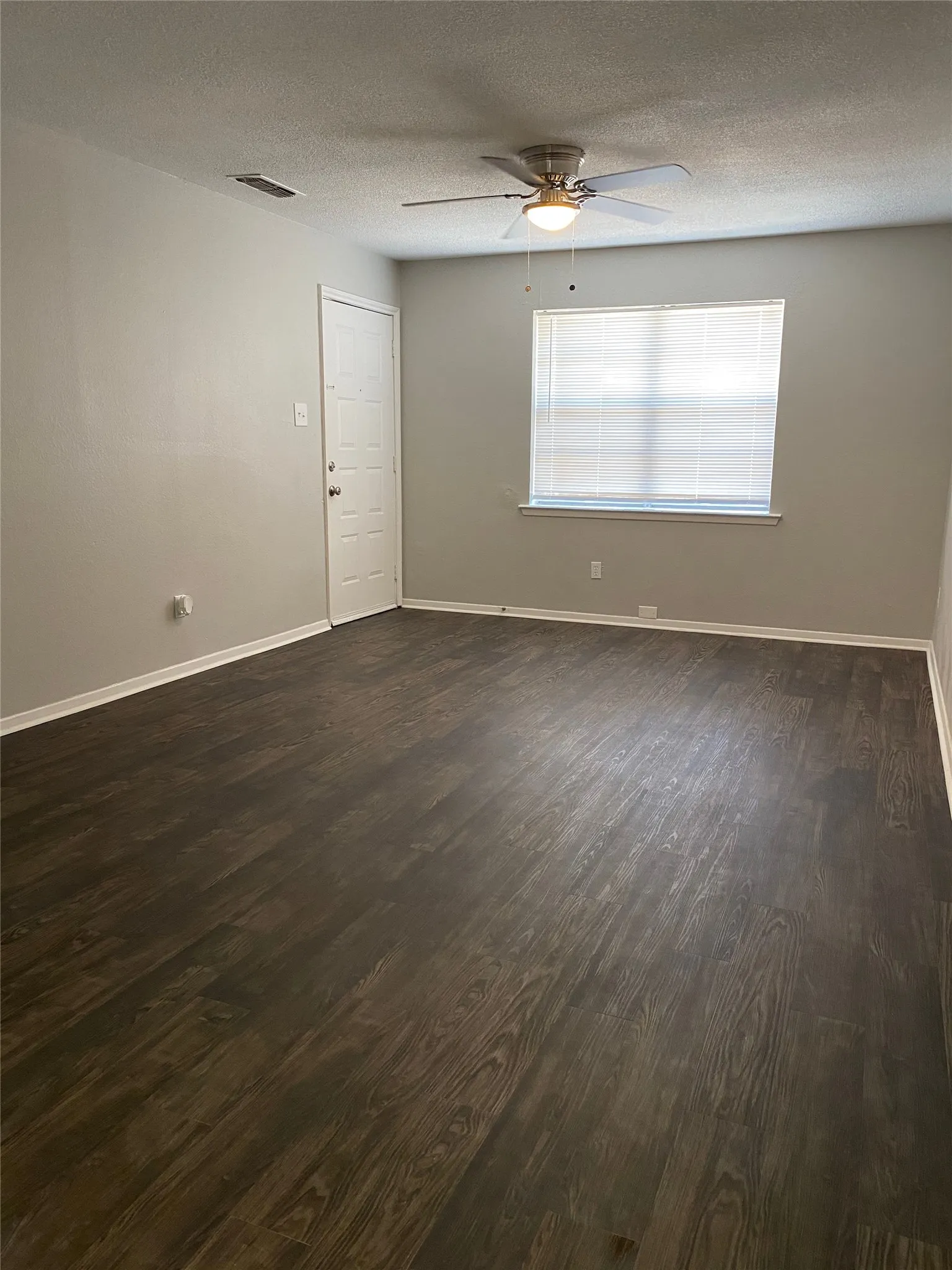 Spacious room featuring wood-finish flooring, a ceiling fan with integrated lighting, a window with blinds, and light-toned wall finishes