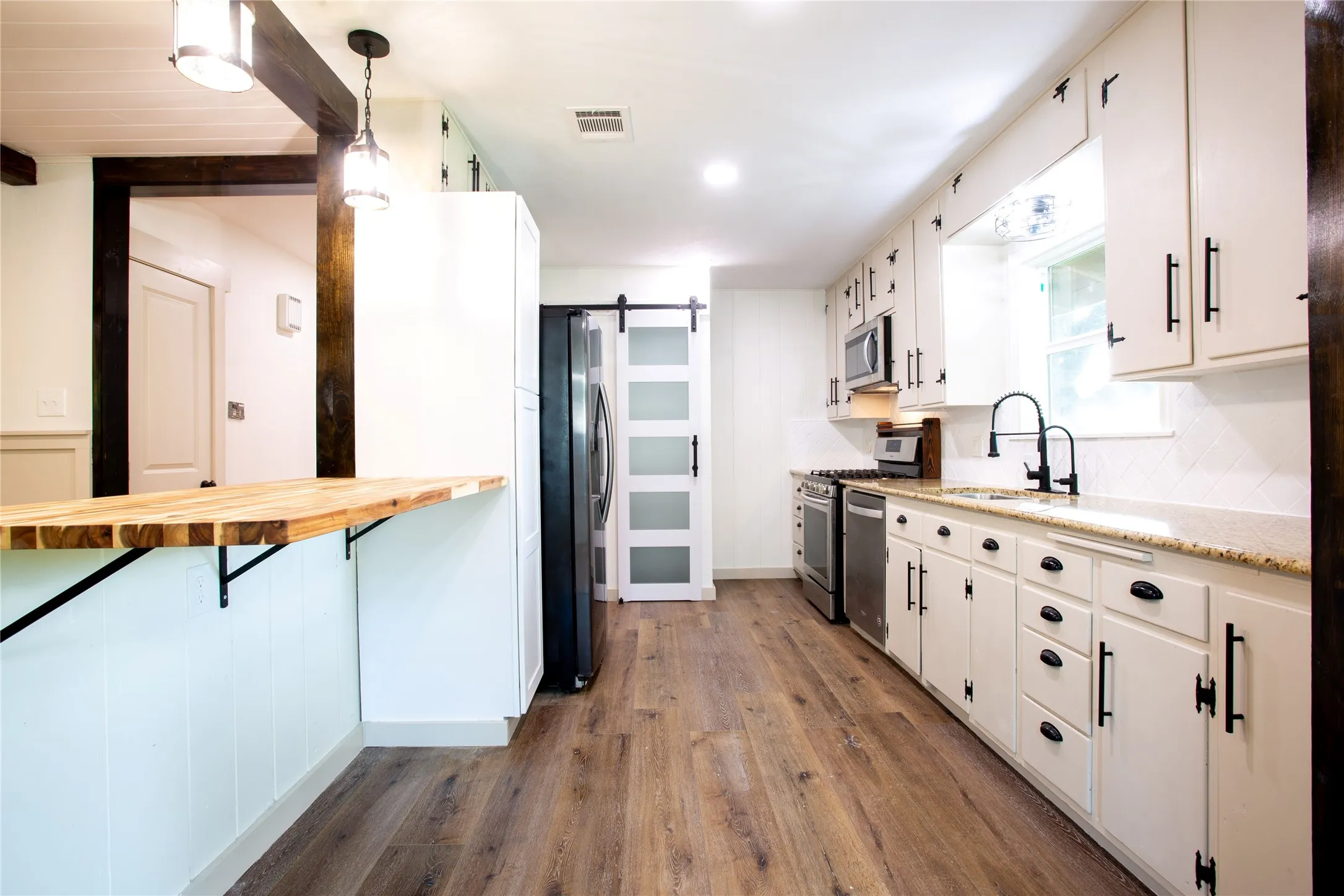 Kitchen featuring wood-finish flooring, white cabinetry with black hardware, stainless steel appliances, and a pantry just past the refrig