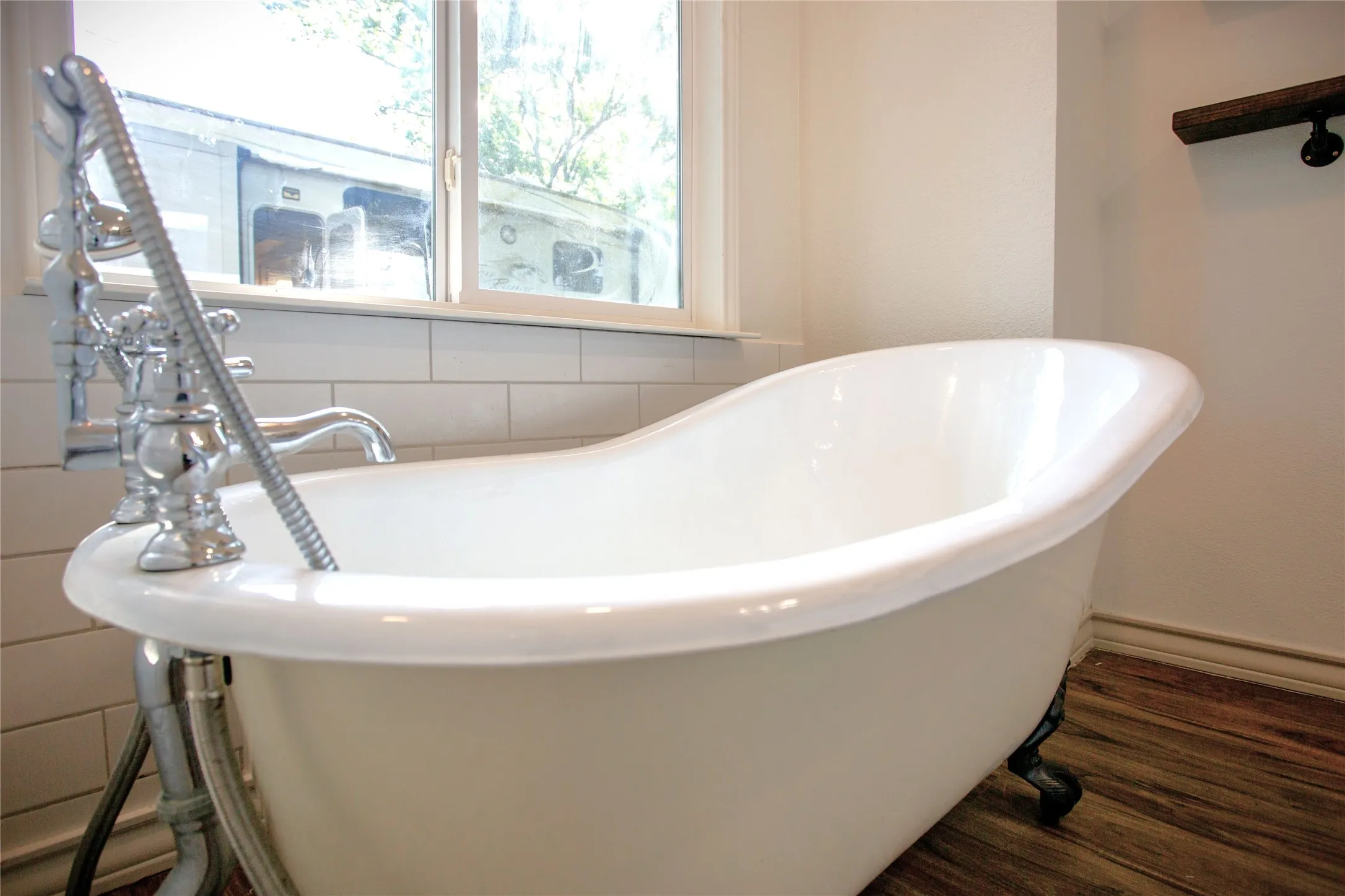 Clawfoot bathtub with chrome fixtures, wood-finish flooring, and subway tile surround