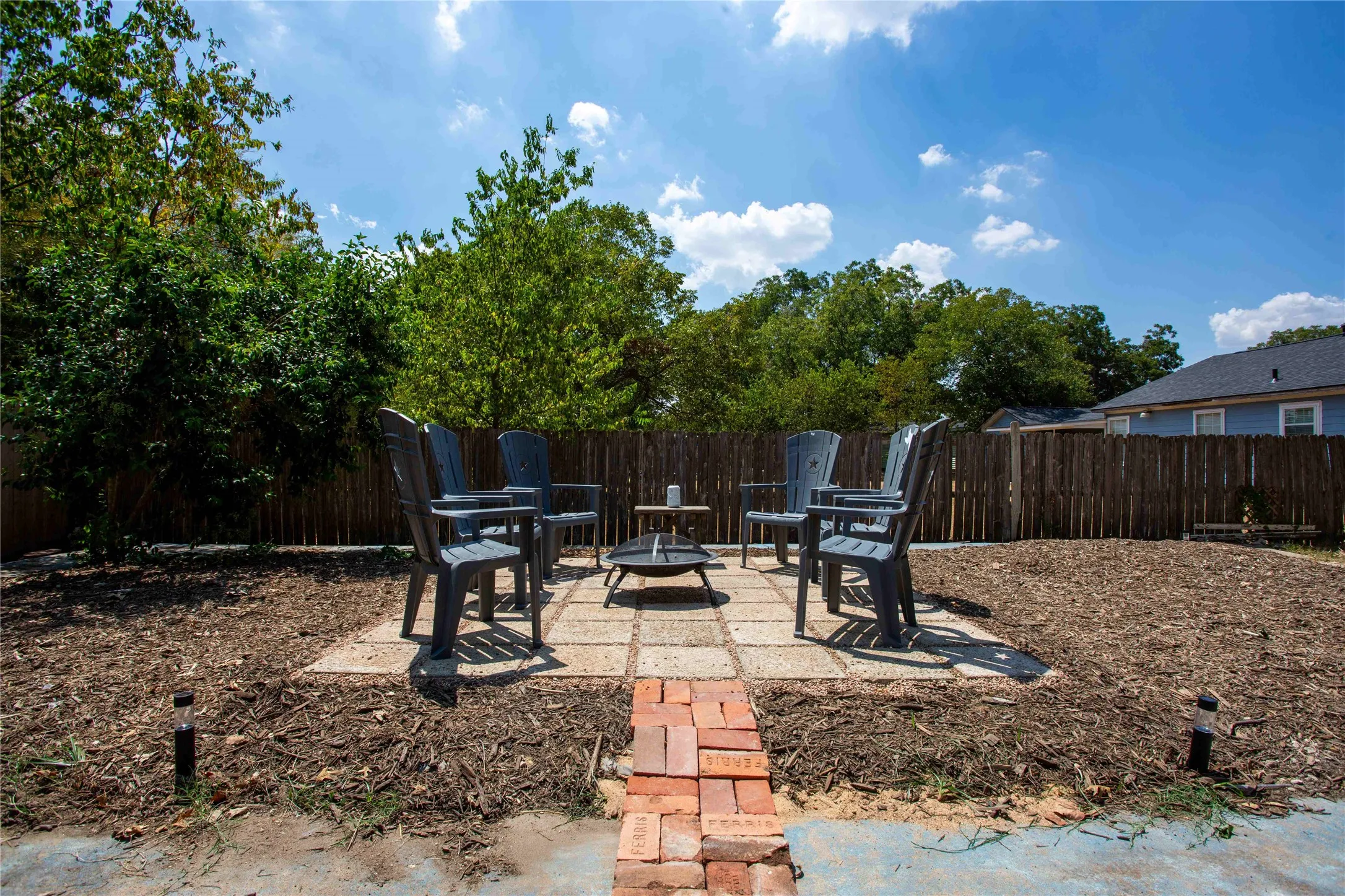 Fire Pit seating area featuring a brick pathway, square paver stones, and a surrounding wood fence