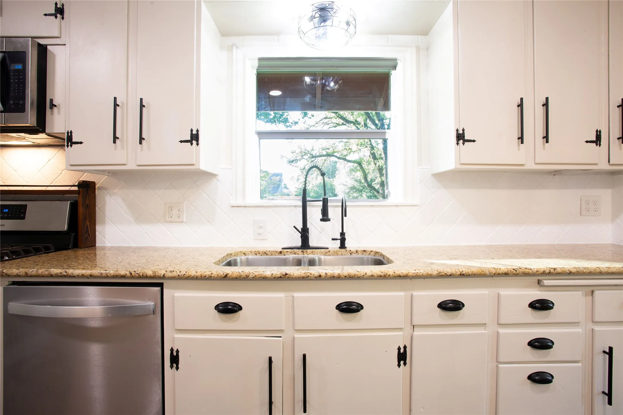 White cabinetry with matte black hardware, stainless steel dishwasher, double basin sink with black faucet, granite countertops, and white tile backsplash