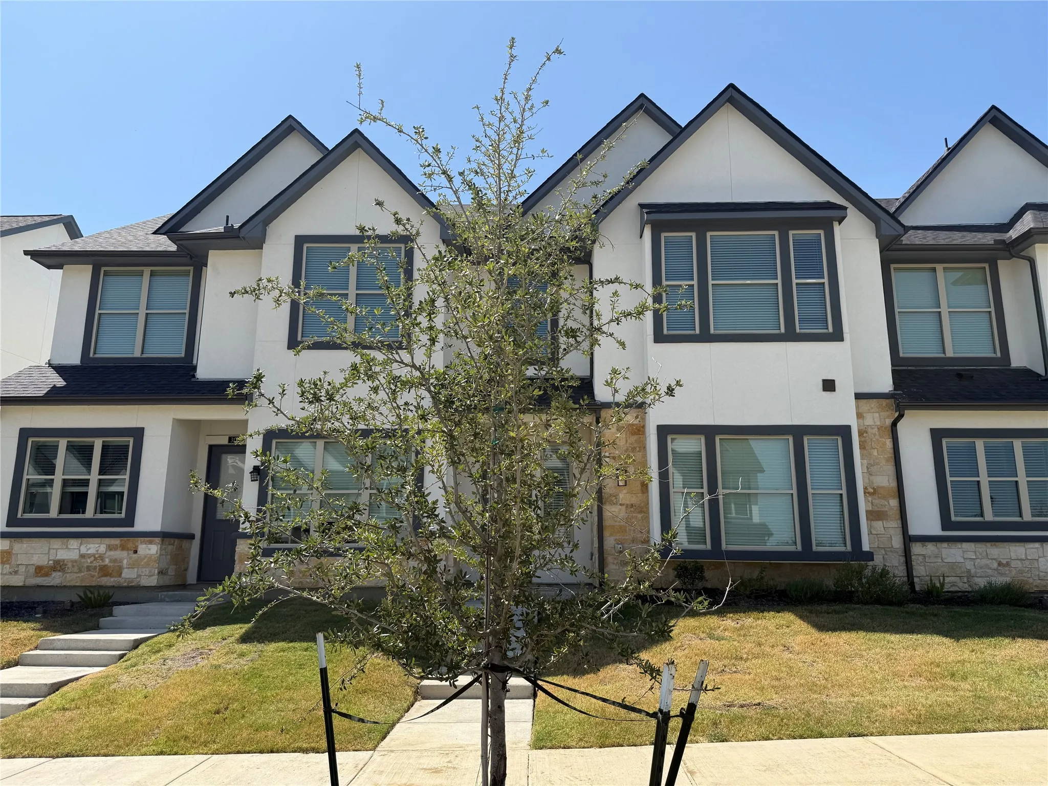 Contemporary townhome with a white facade, dark trim, and stone accents