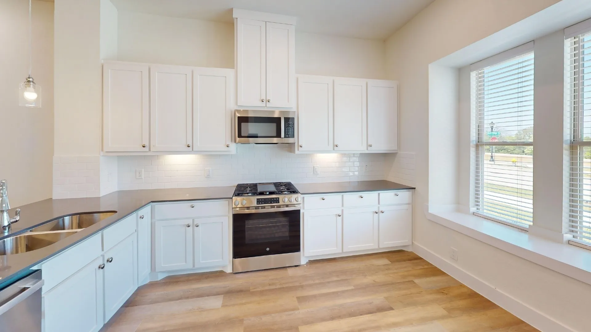 Kitchen featuring white shaker cabinetry, stainless steel appliances, dark countertops, a white subway tile backsplash, and wood-finish flooring