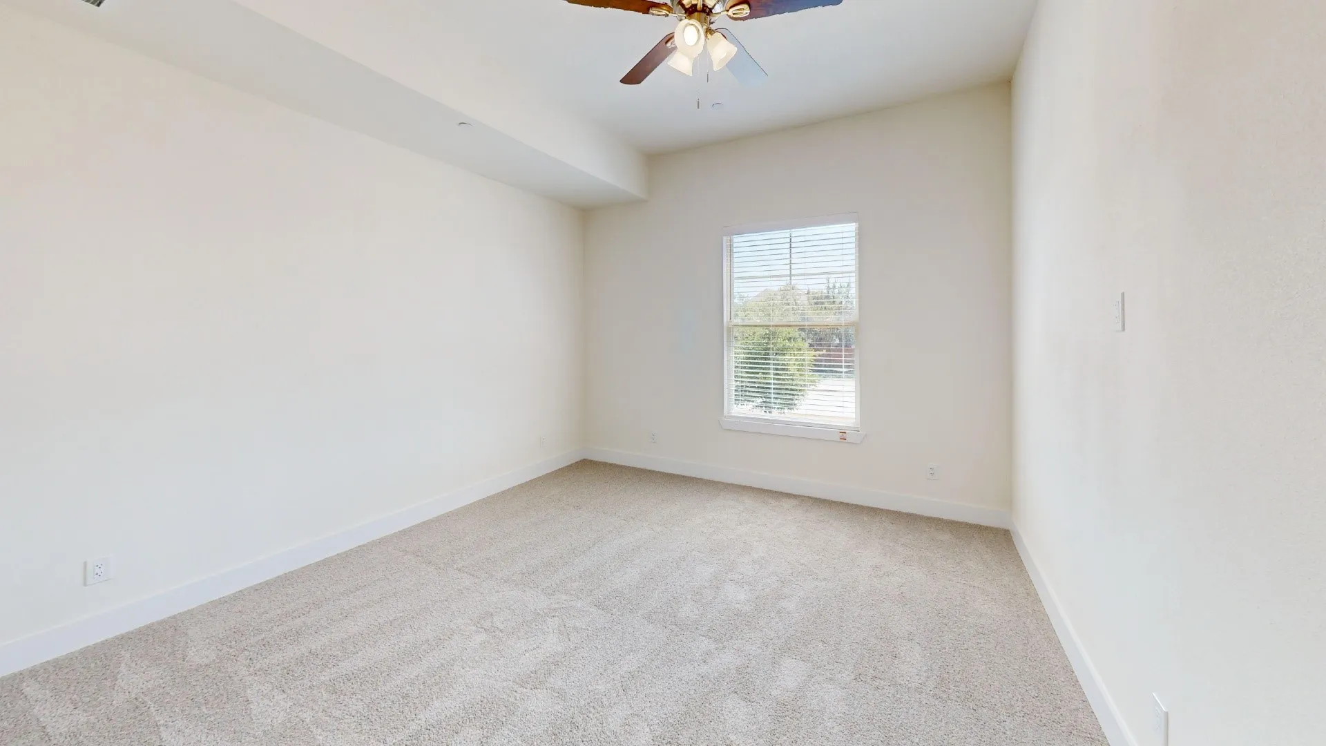 Bright bedroom featuring neutral carpet flooring, a ceiling fan with integrated lighting, and a large window allowing natural light throughout the space