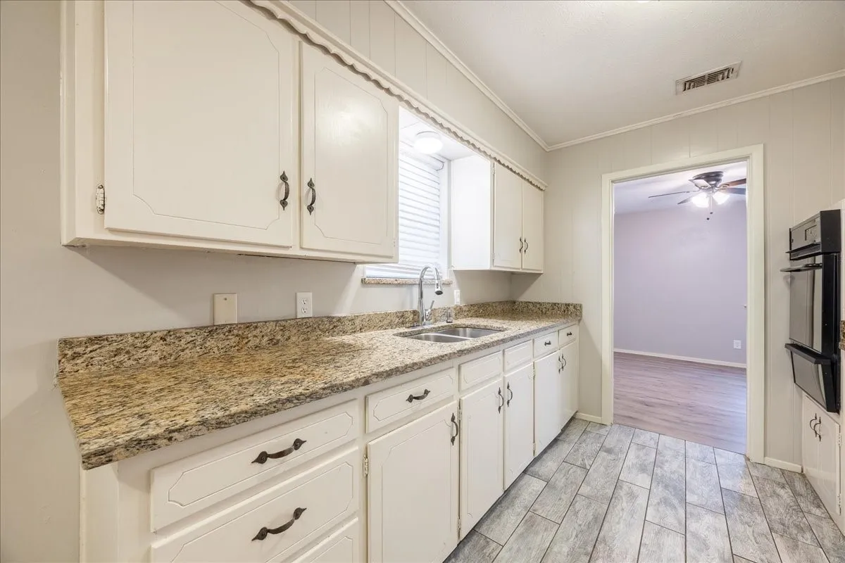 White cabinetry with decorative hardware, stone-finish countertops, dual basin sink with a chrome faucet, integrated double wall ovens, and wood-look plank flooring