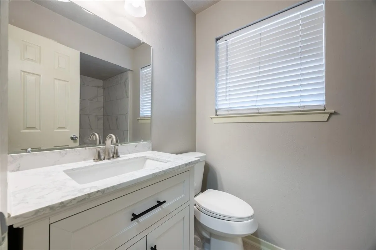 White vanity with black hardware, white countertop, undermount sink, and brushed nickel faucet