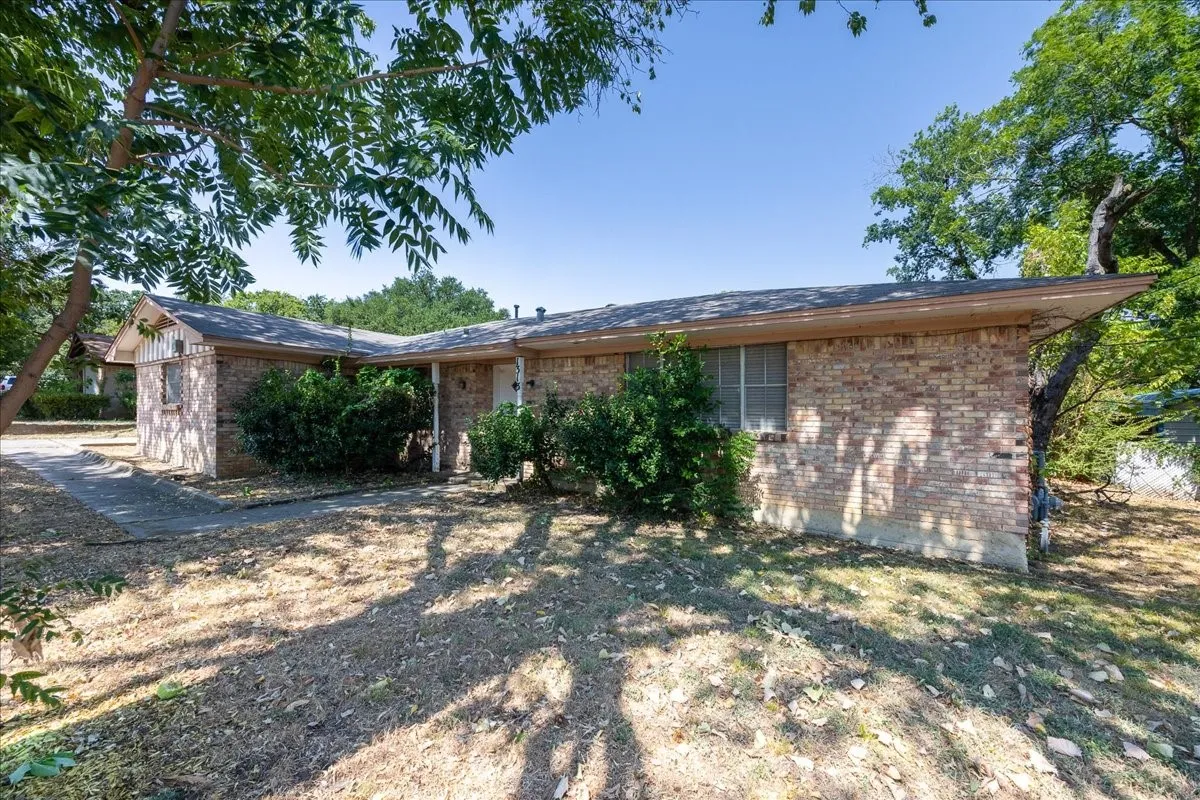 Brick exterior, mature trees, concrete pathway, attached carport, and established shrubbery