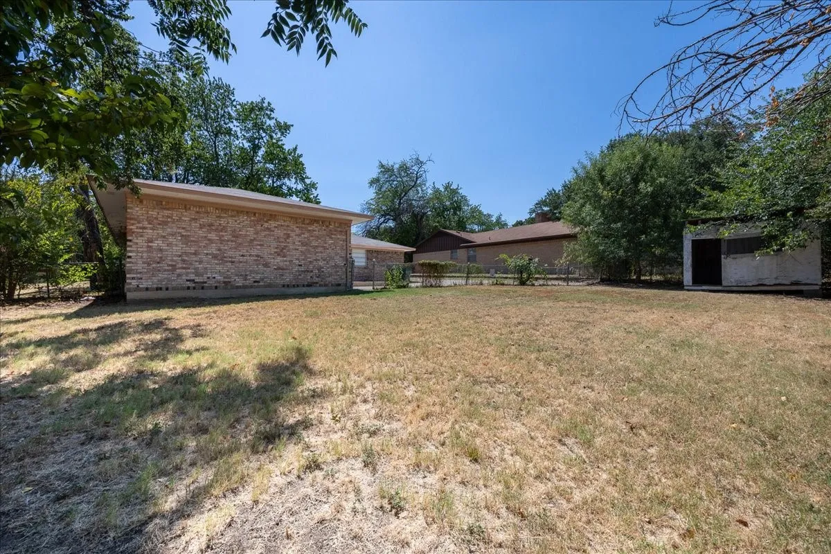 Expansive outdoor area featuring a brick-clad structure, a separate storage shed, and mature perimeter trees
