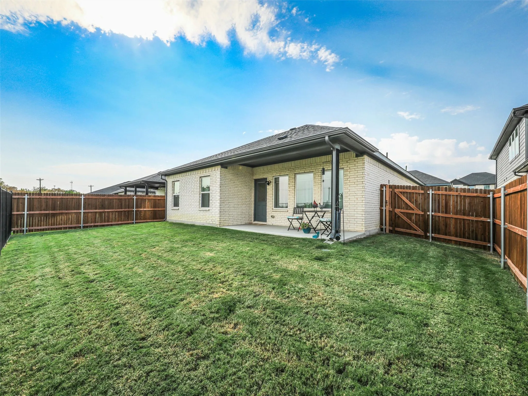 Expansive fenced backyard featuring a covered concrete patio, light-colored brick exterior, and dark-toned roofing