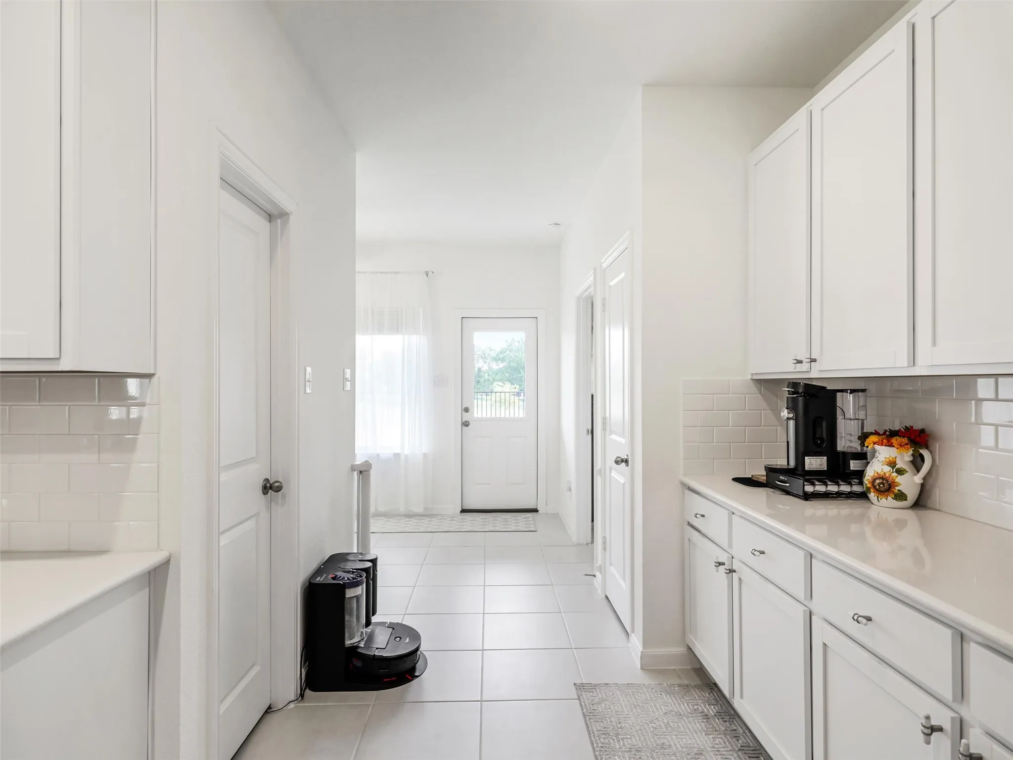 White cabinetry with chrome hardware, subway tile backsplash, light-toned countertops, and tile flooring