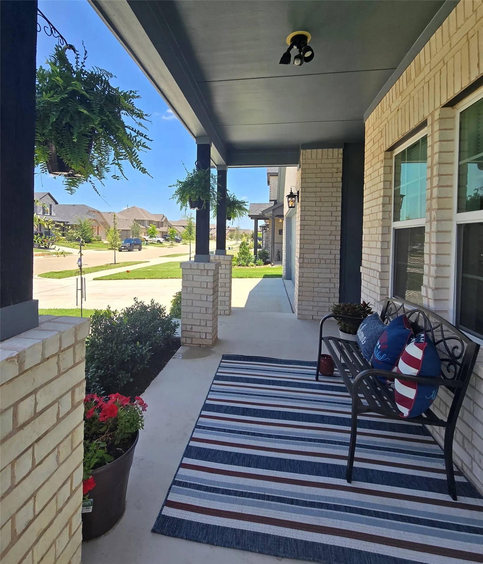 Covered front porch featuring brick columns, recessed lighting, and a concrete surface